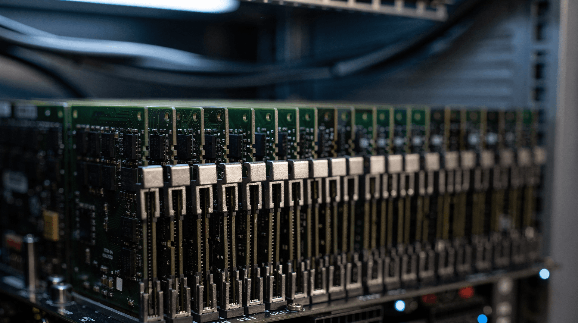 Close-up of stacked memory modules in a server rack, with a datacenter aisle blurred in cool blue light behind.
