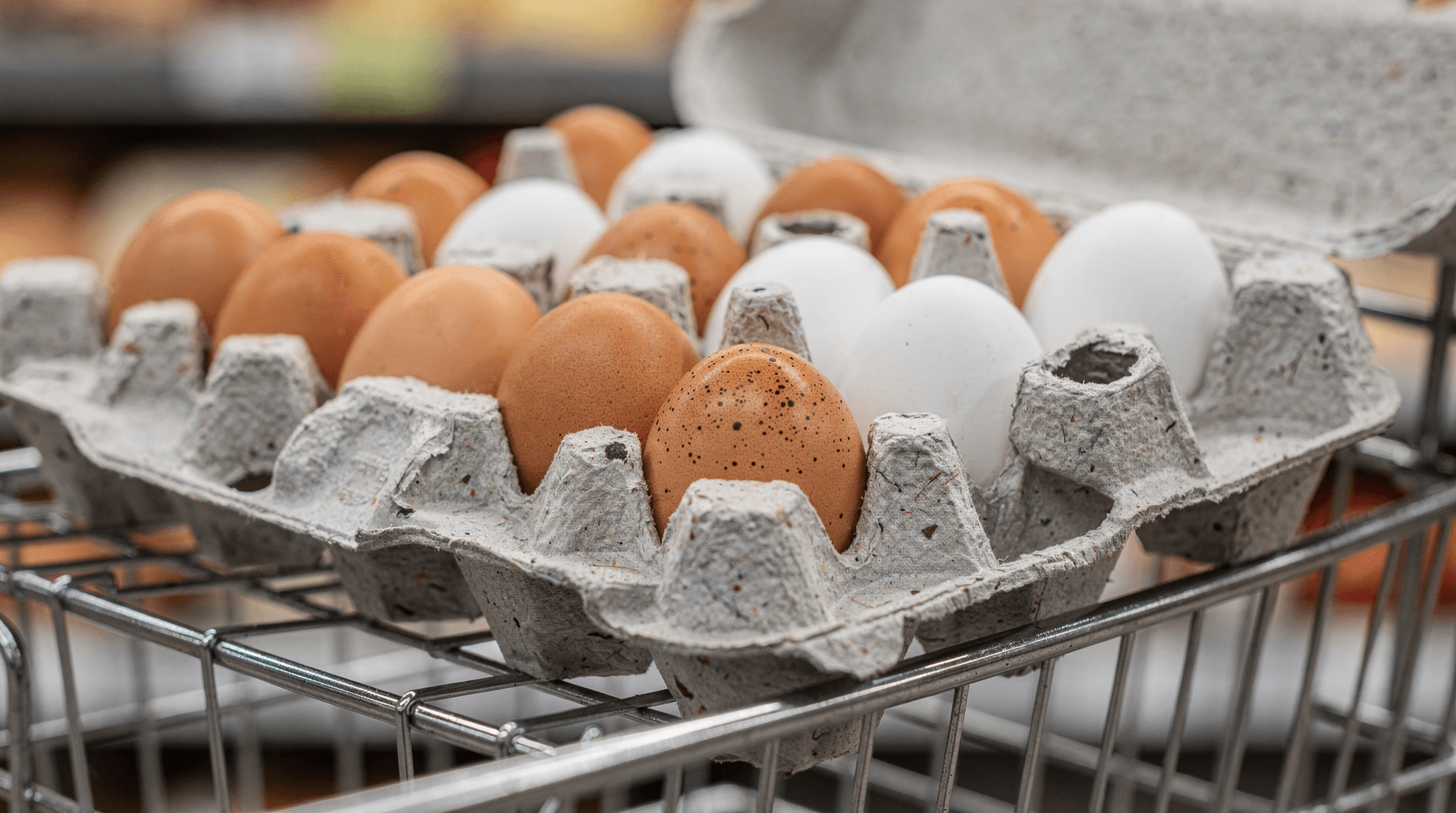 Close-up of brown and white eggs in an open paperboard carton in a wire shopping basket