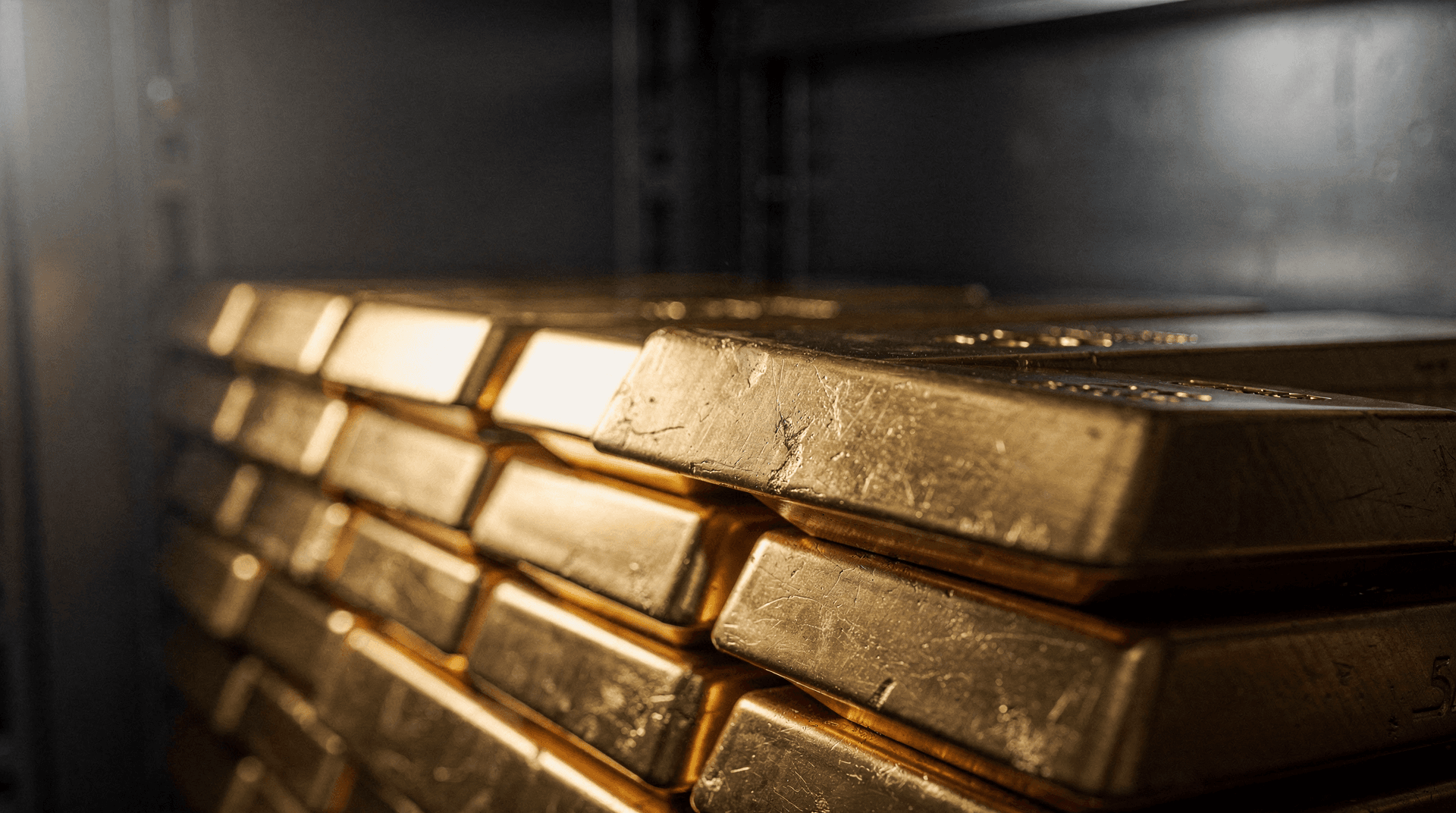 Several stacked gold bars, some showing imperfections and light reflections, against a dark, slightly blurry background.