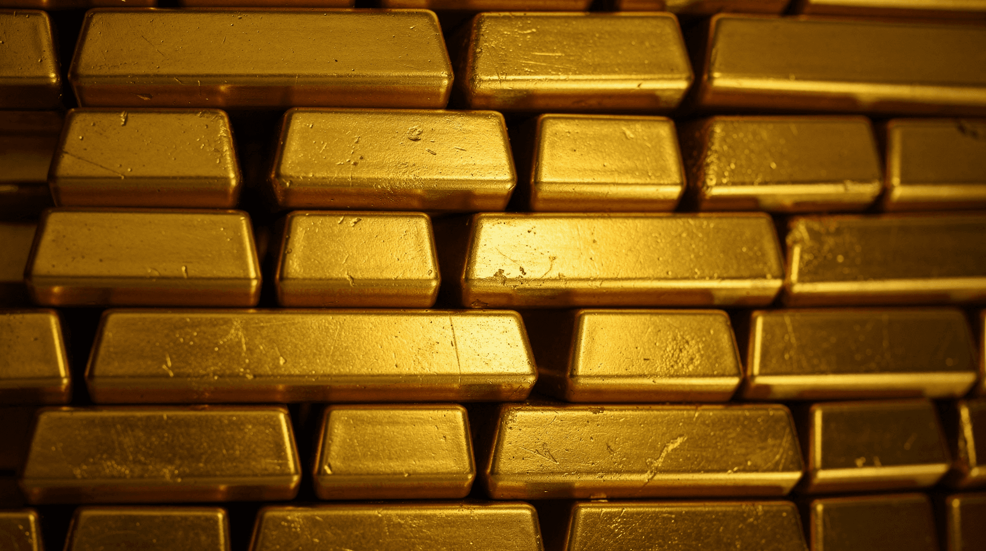 Close-up, top-down shot of multiple shiny gold bars stacked in horizontal rows, filling the frame from edge to edge.