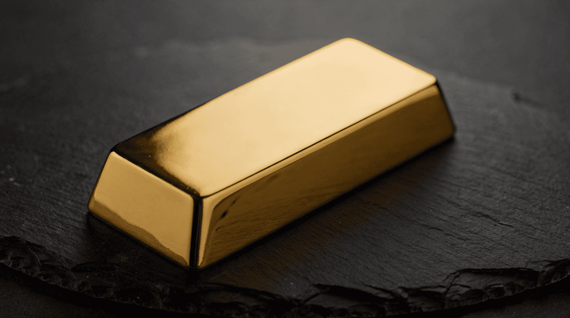 Close-up, slightly high angle, on a rectangular gold bar with smooth, reflective surfaces, resting on a dark slate surface