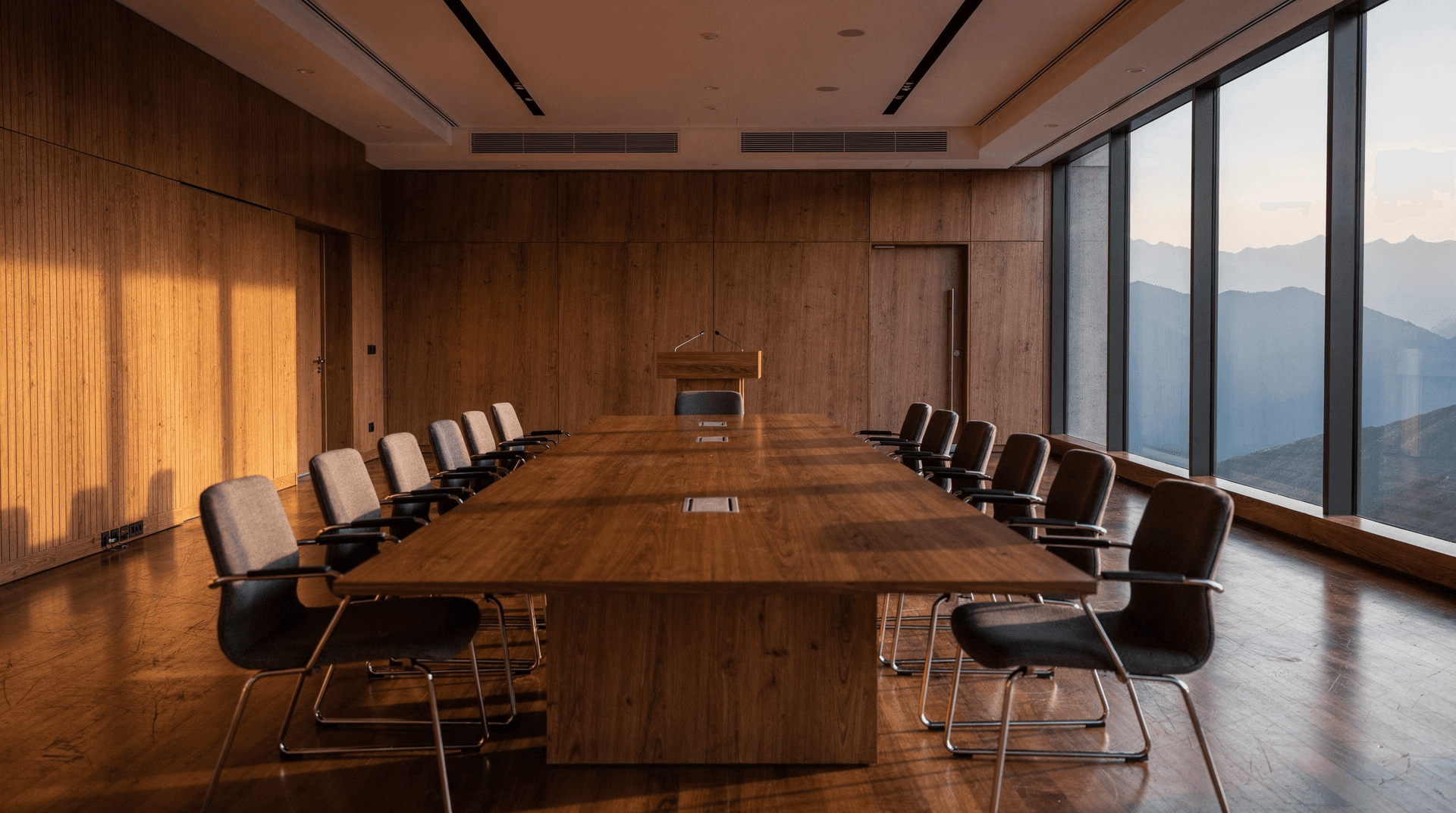 Empty wood-paneled conference hall with table and chairs facing a podium
