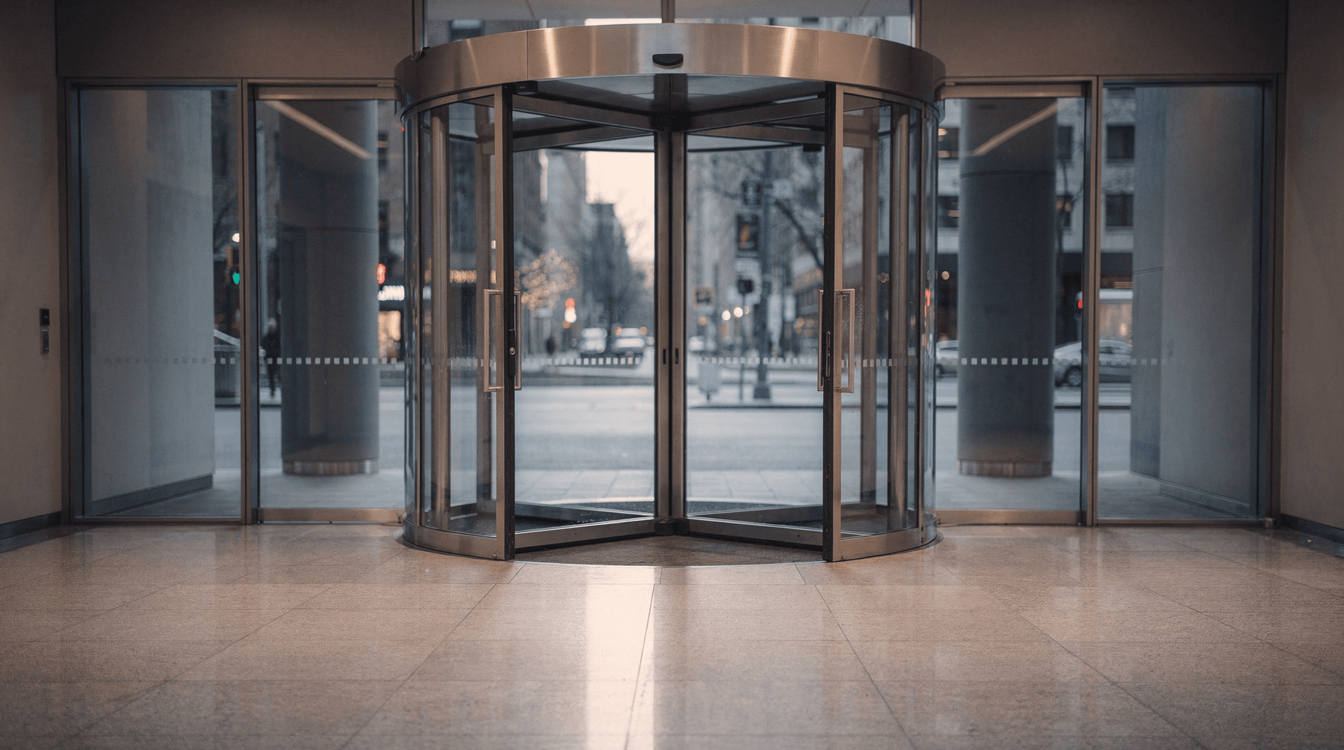 A glass revolving door stands motionless in an empty office-tower lobby at dawn