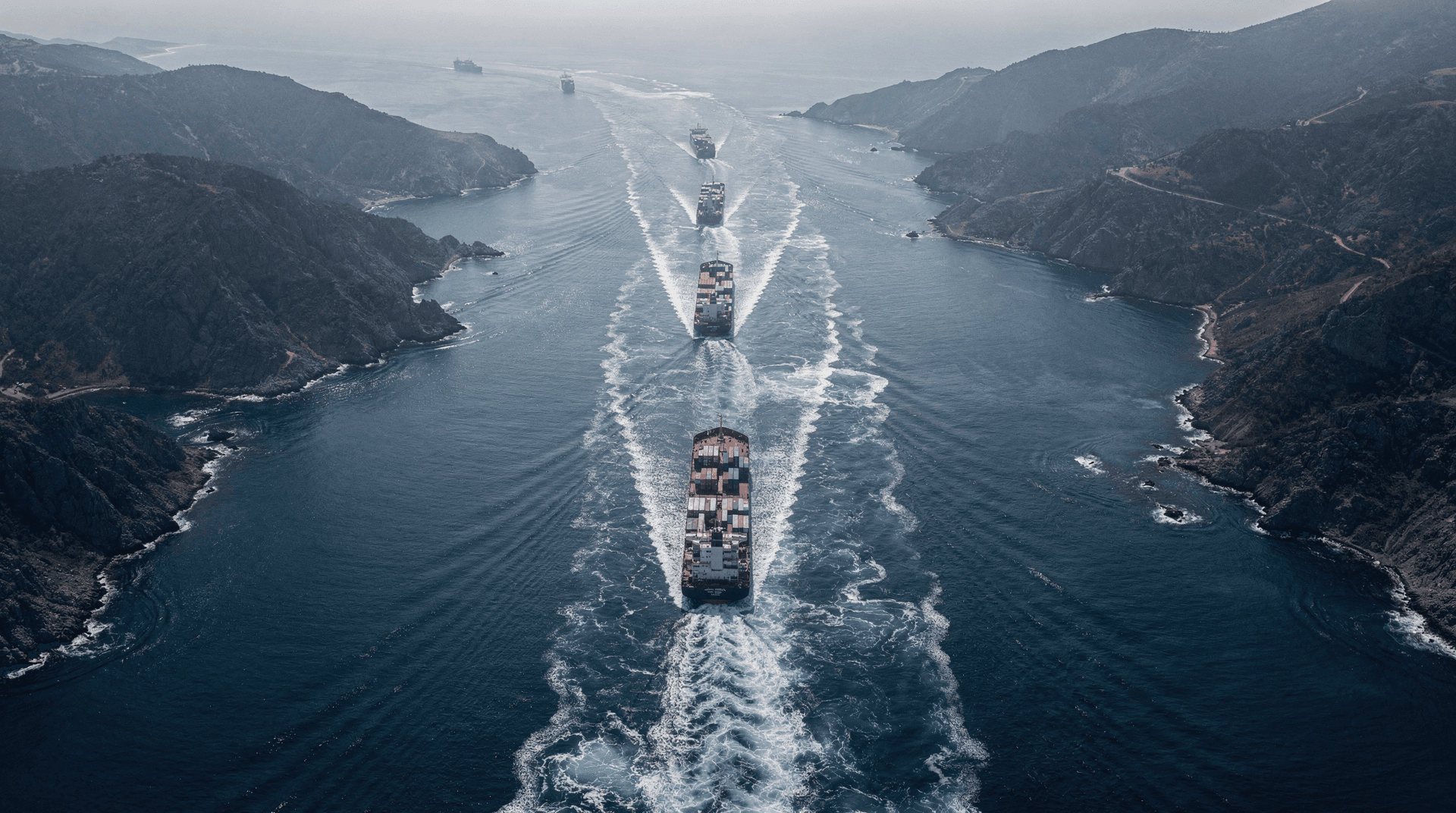 Aerial perspective of a strait with multiple ships leaving wakes, showing maritime trade routes