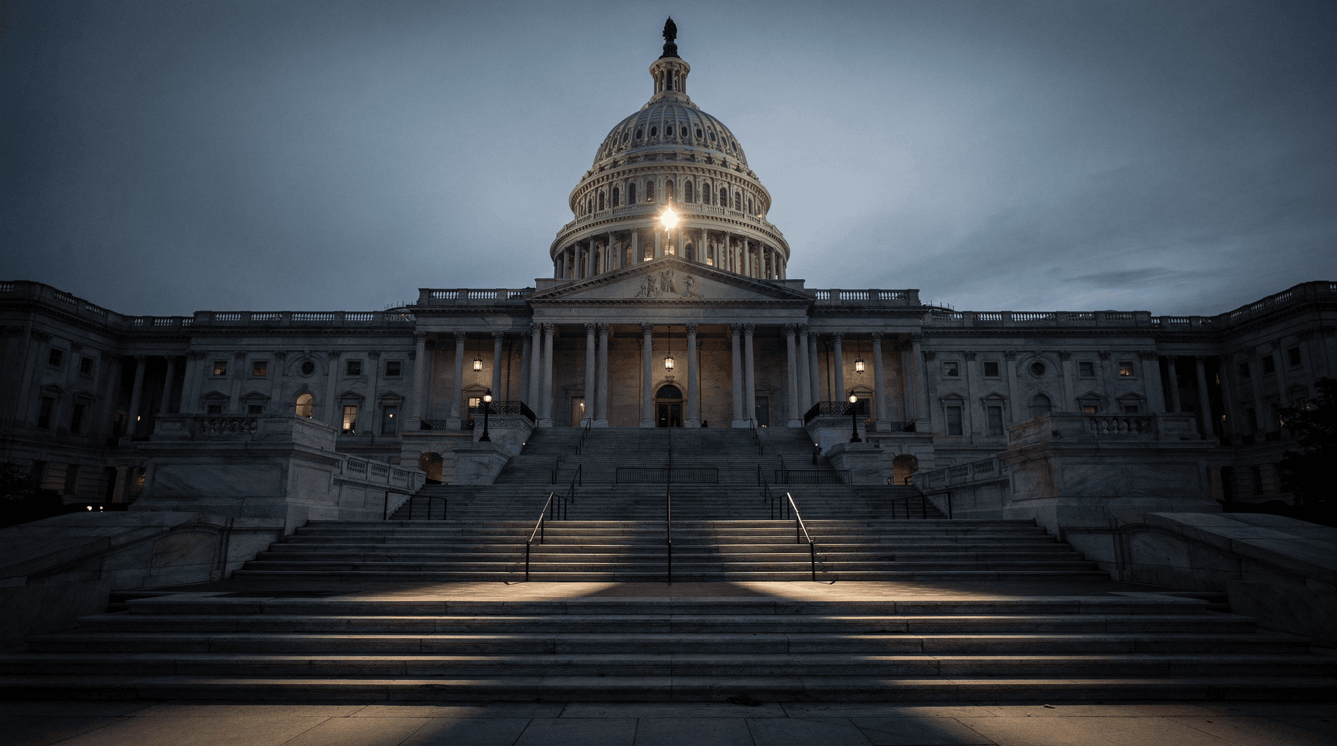 The US Capitol Building at dusk, illuminated, with its dome and grand staircase prominent against a darkening sky.