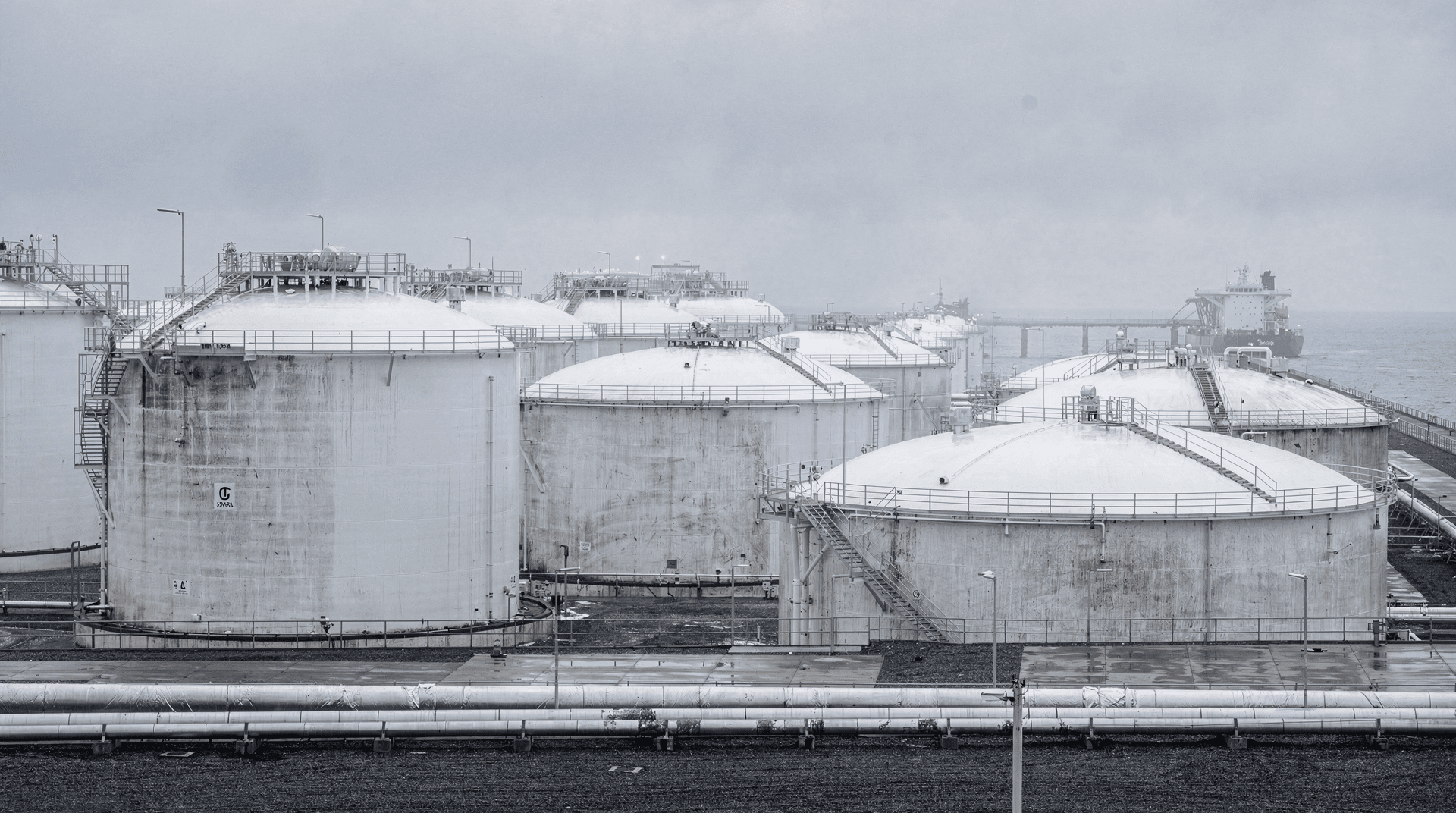 Rows of white LNG storage tanks at a coastal import terminal under an overcast winter sky
