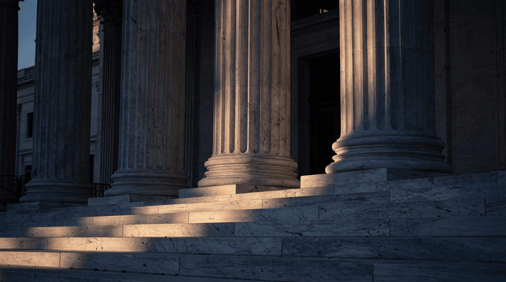 Grand marble courthouse columns at dusk, shadows dividing the facade into three uneven sections