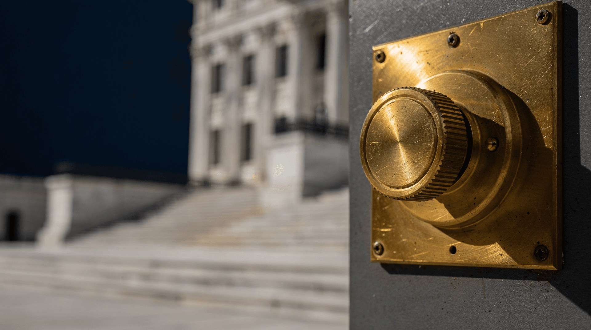 Brass rate-adjustment dial in warm light with a blurred marble government building facade behind it
