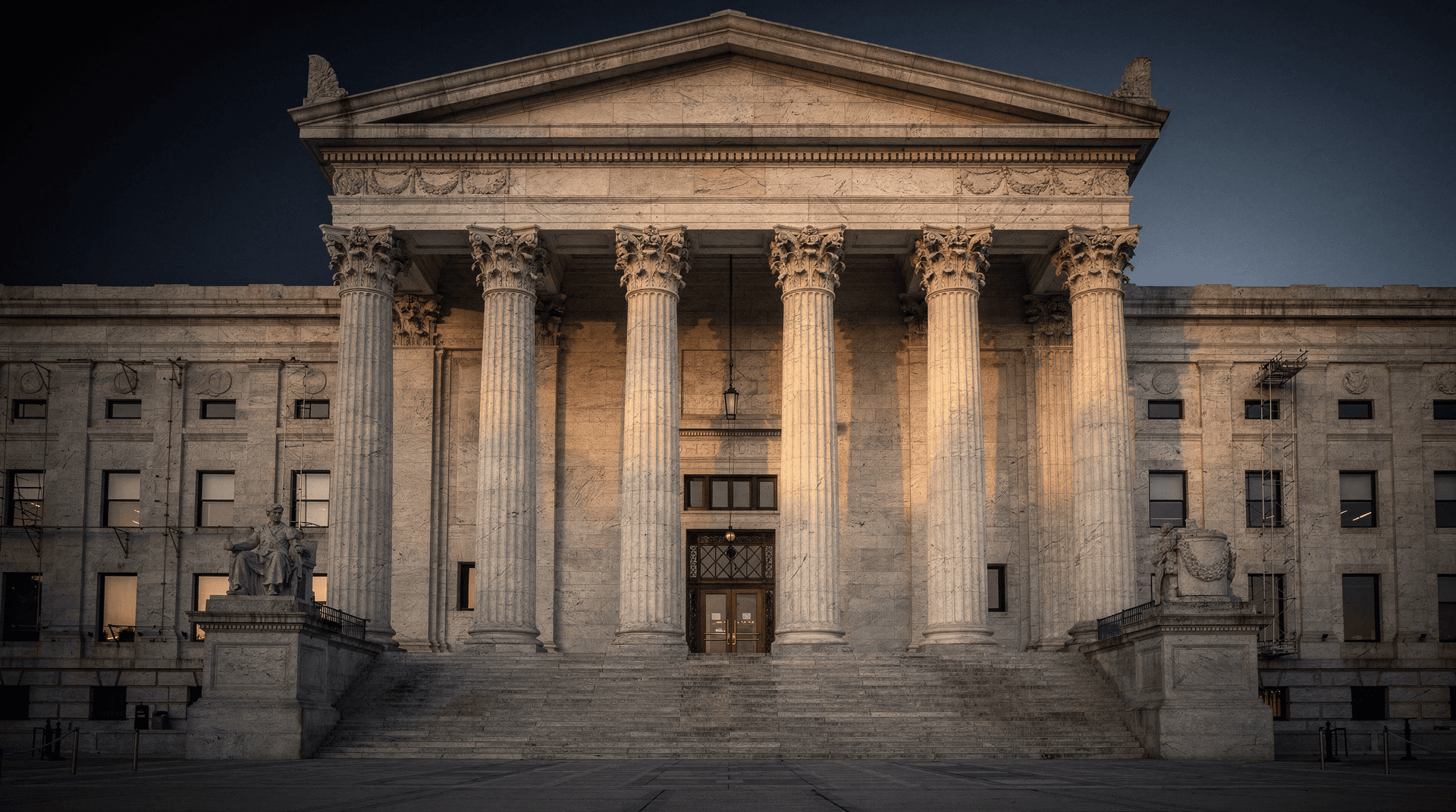 Stone columns of a government building glow gold against a darkening navy sky at dusk.
