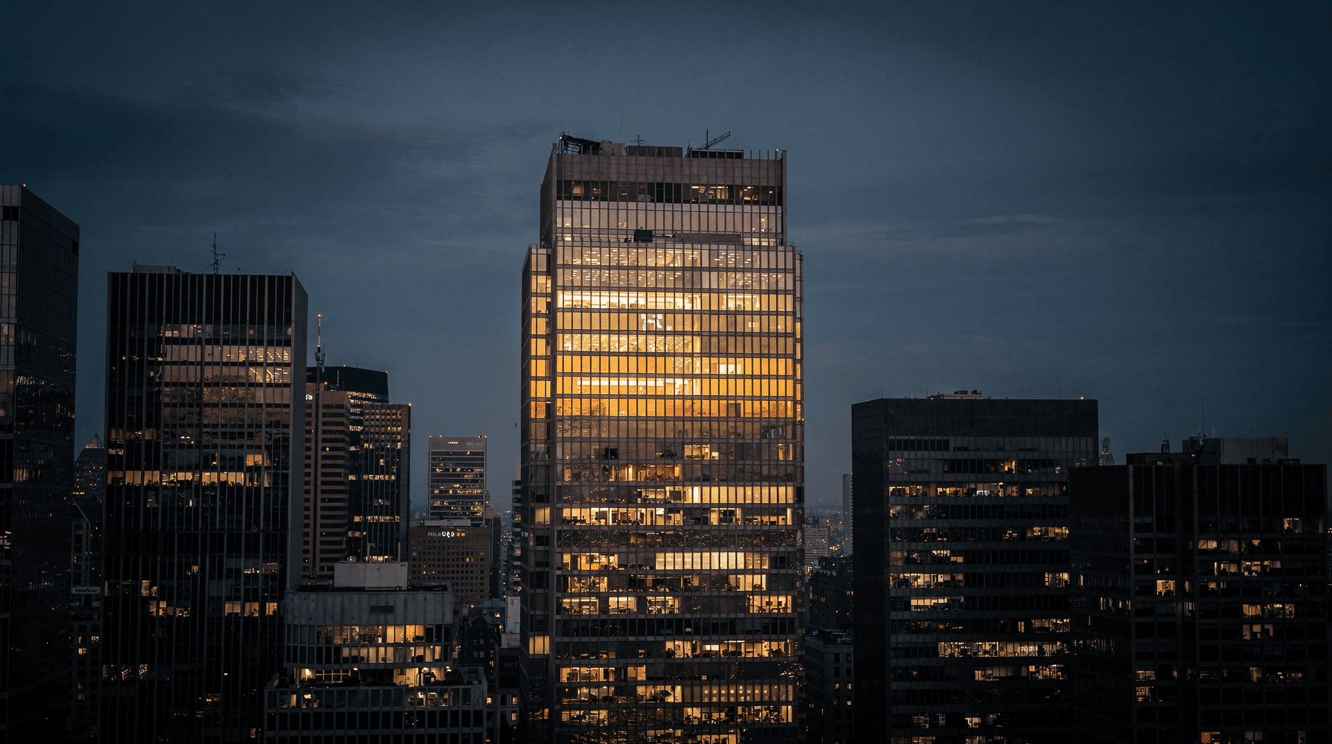 a single brightly lit glass office tower among dimmer ones