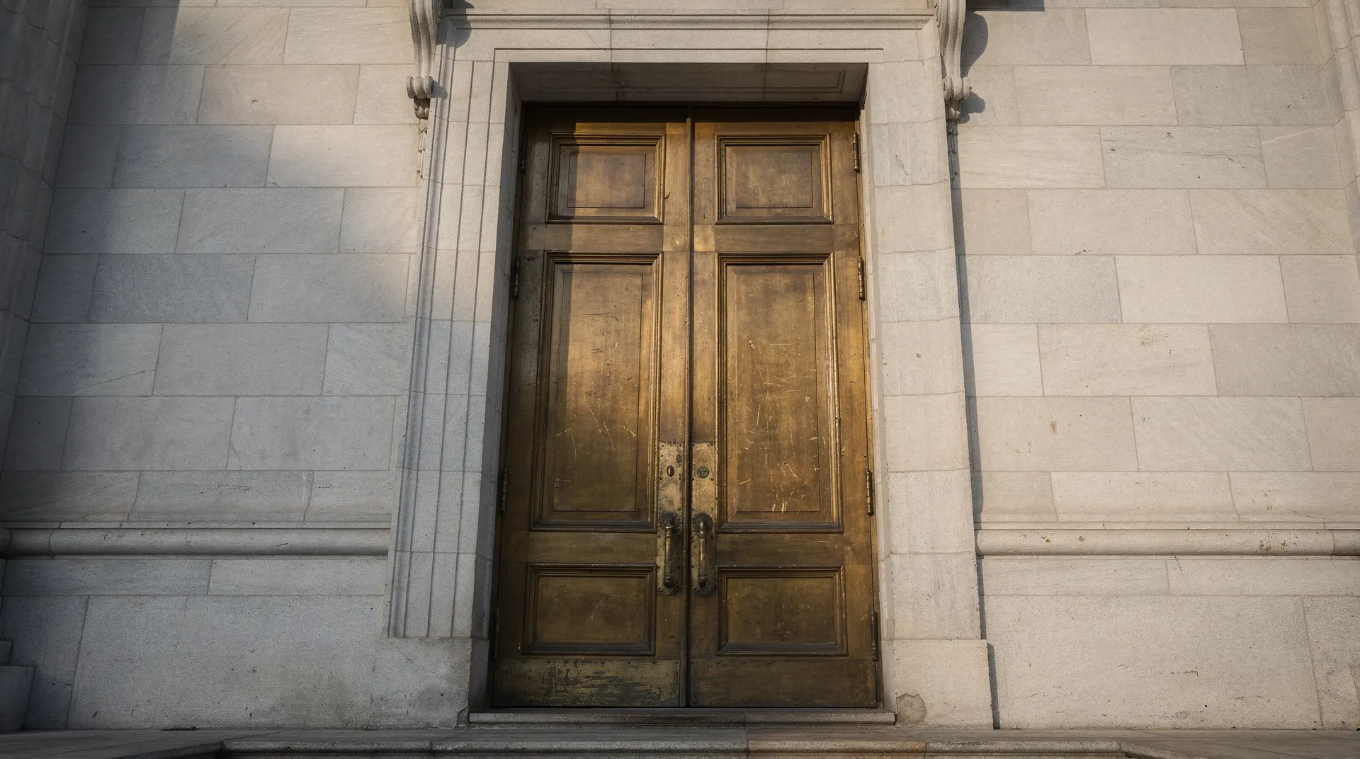 Closed bronze doors sit between shadowed stone columns in a tight architectural crop.
