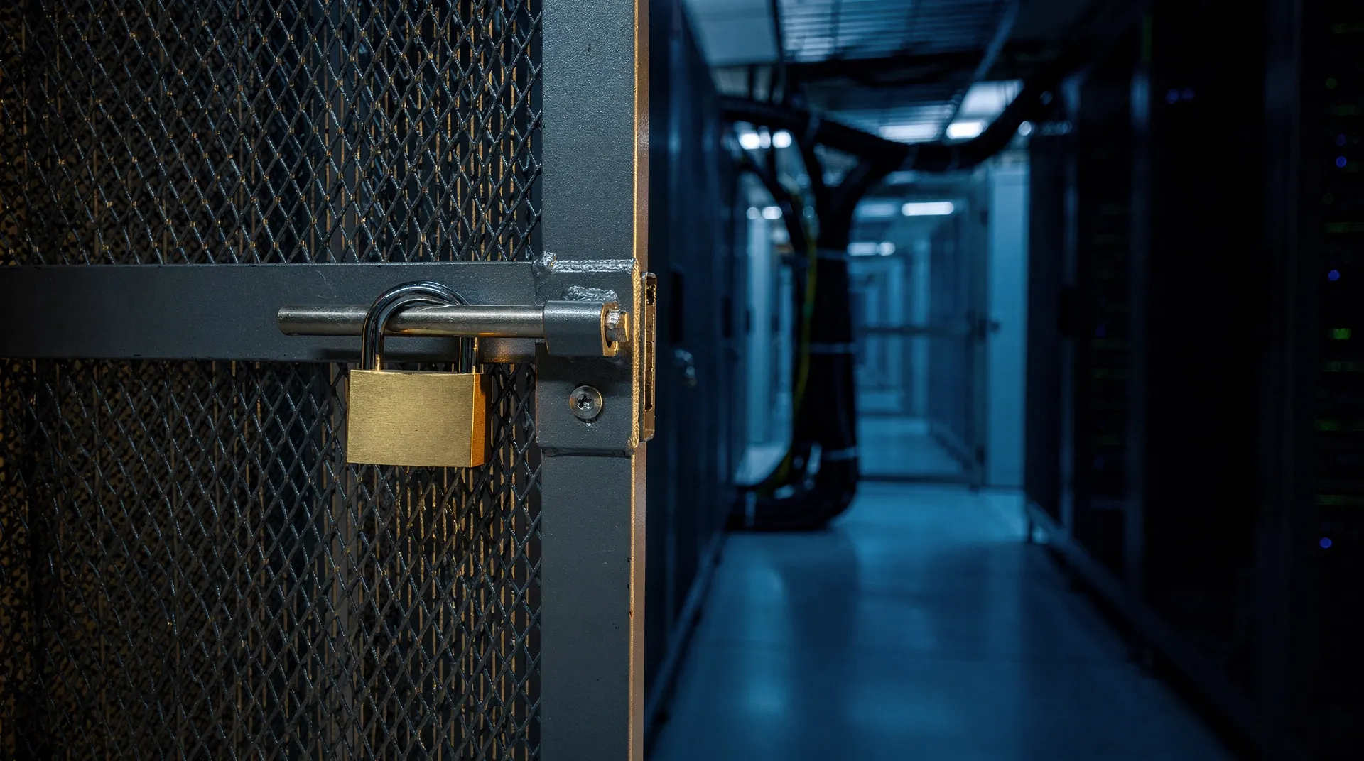 A padlock secures a mesh cage around server racks receding into a dim blue data-center aisle.