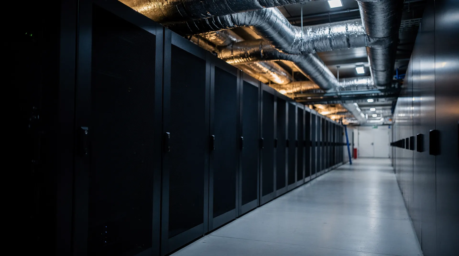 Unmarked server racks and cooling pipes recede along a dimly lit data-center aisle.