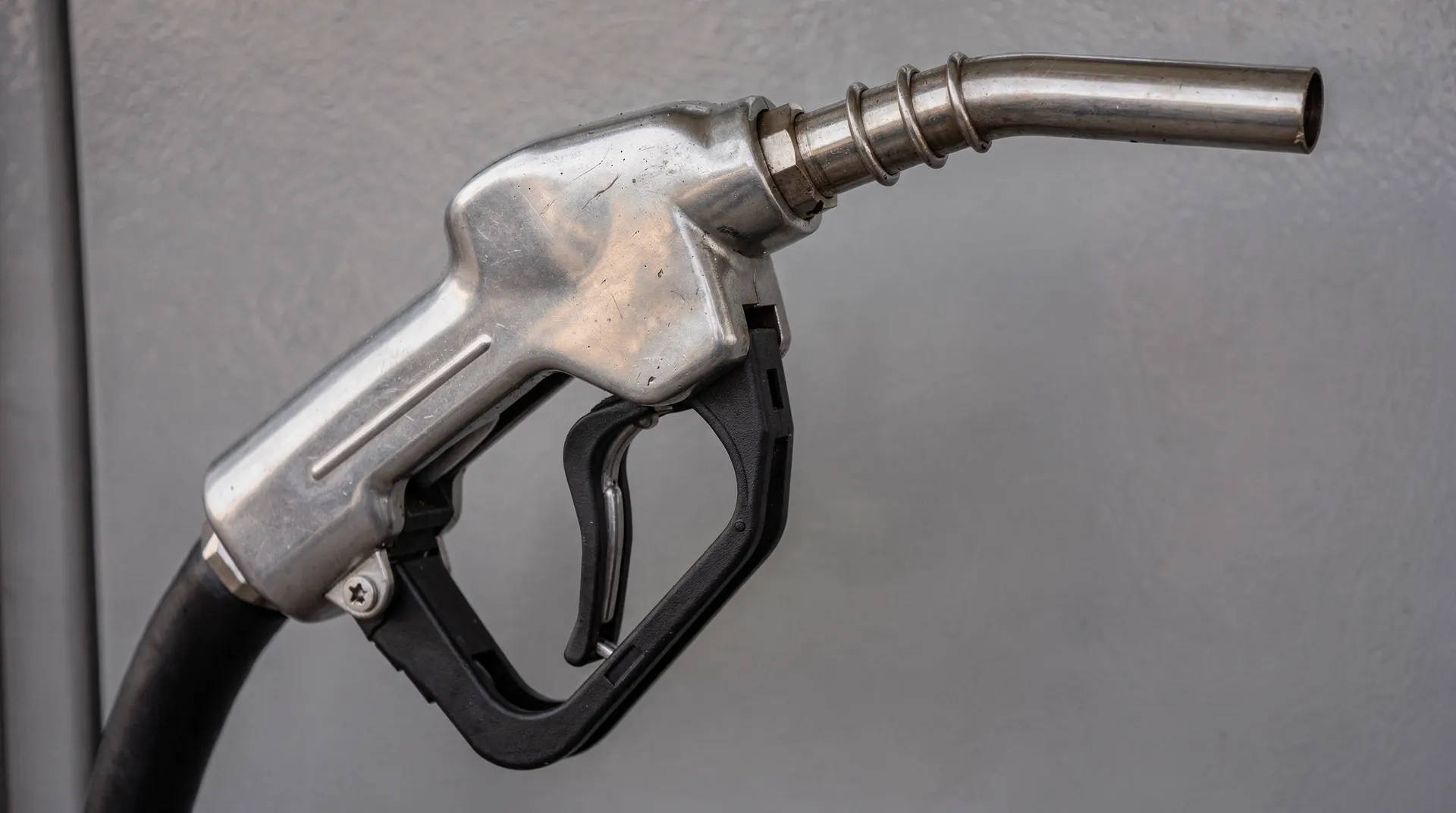 An unbranded gasoline pump nozzle and hose against a plain station wall.