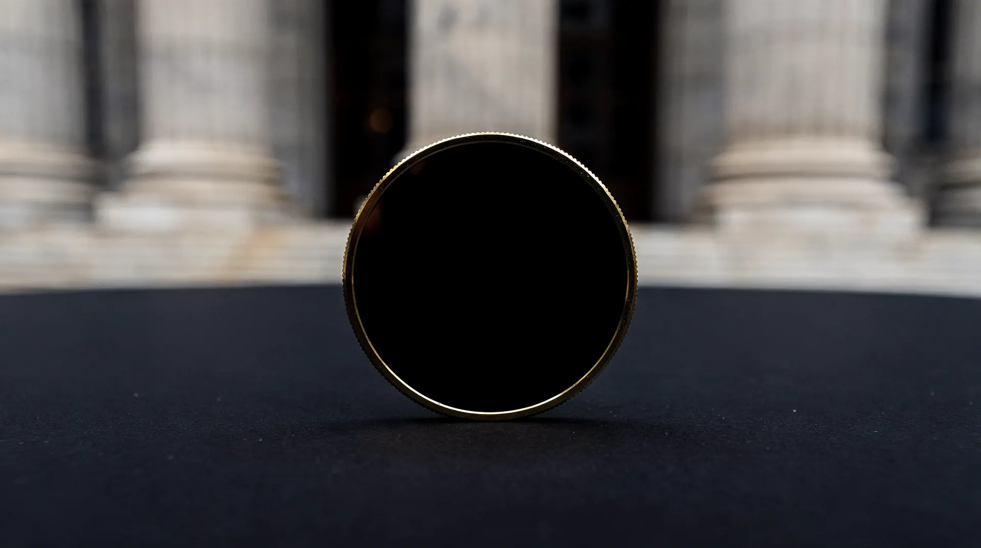 A blank-faced metallic token stands before blurred stone columns in low light.