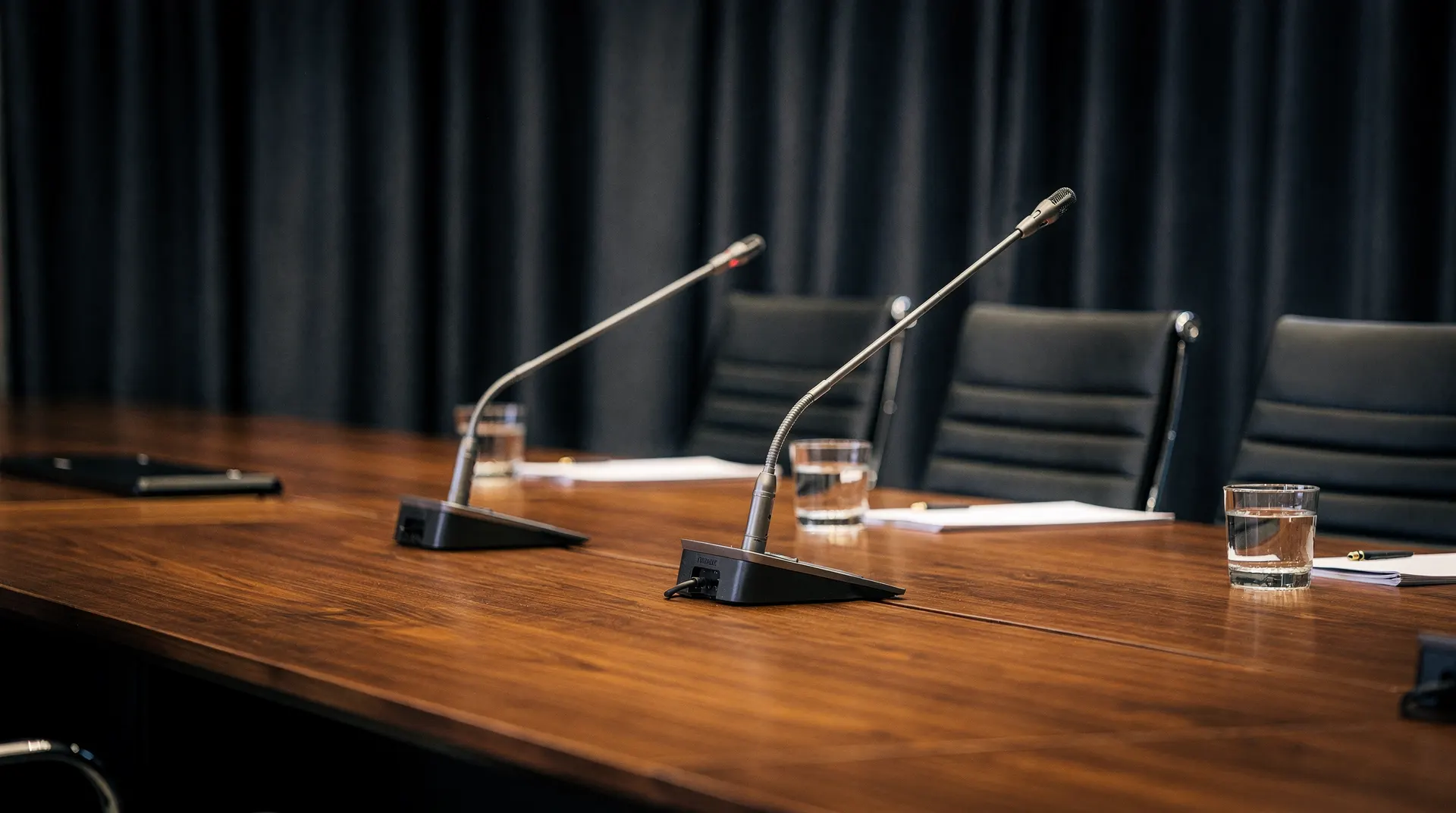 An empty conference lectern holds two separated microphones before rows of softly blurred chairs.
