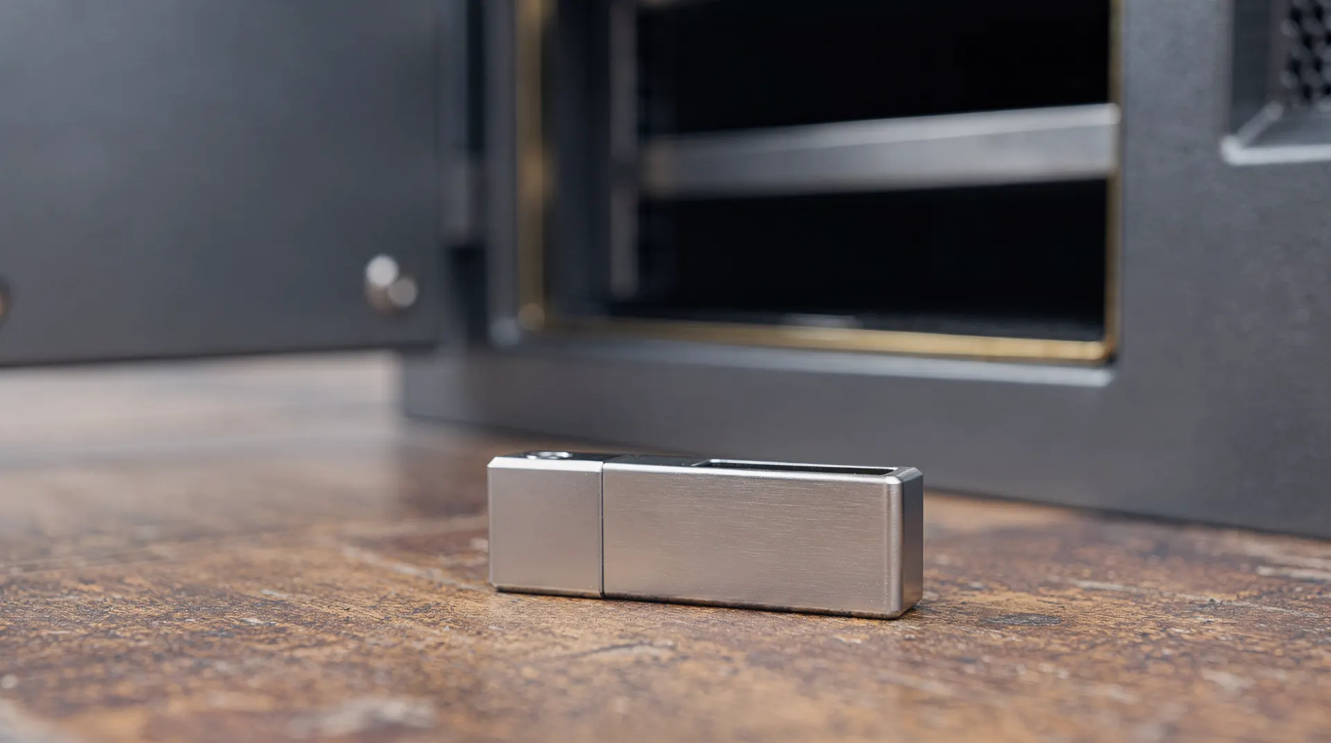 An unmarked hardware wallet sits on a tabletop outside an open vault compartment.