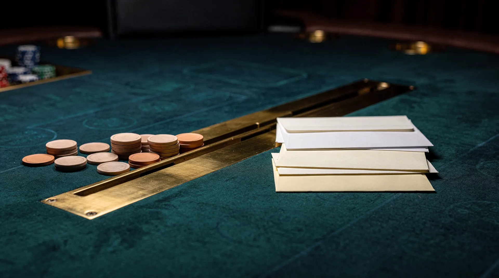 Plain gaming chips and sealed blank envelopes sit on opposite sides of a brass divider on a casino table.