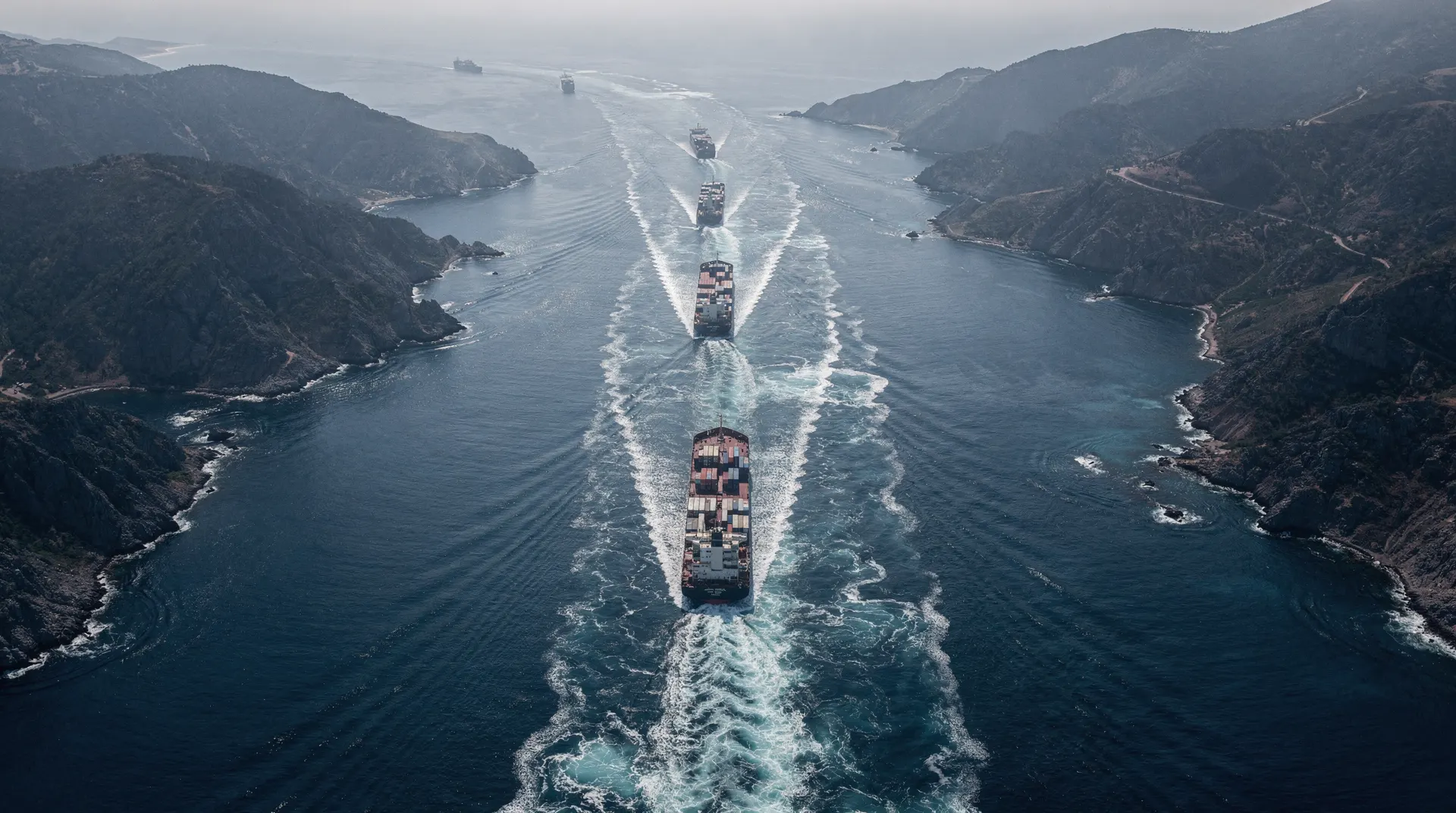 Aerial perspective of a strait with multiple ships leaving wakes, showing maritime trade routes