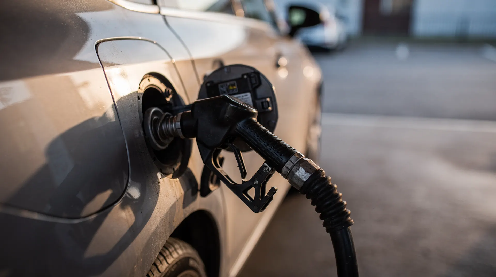 A gasoline nozzle fills a car at a quiet station in warm late-summer light.