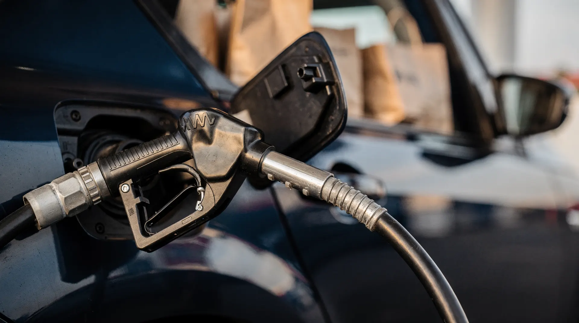 A fuel-pump nozzle fills a car, with grocery bags visible through the window.