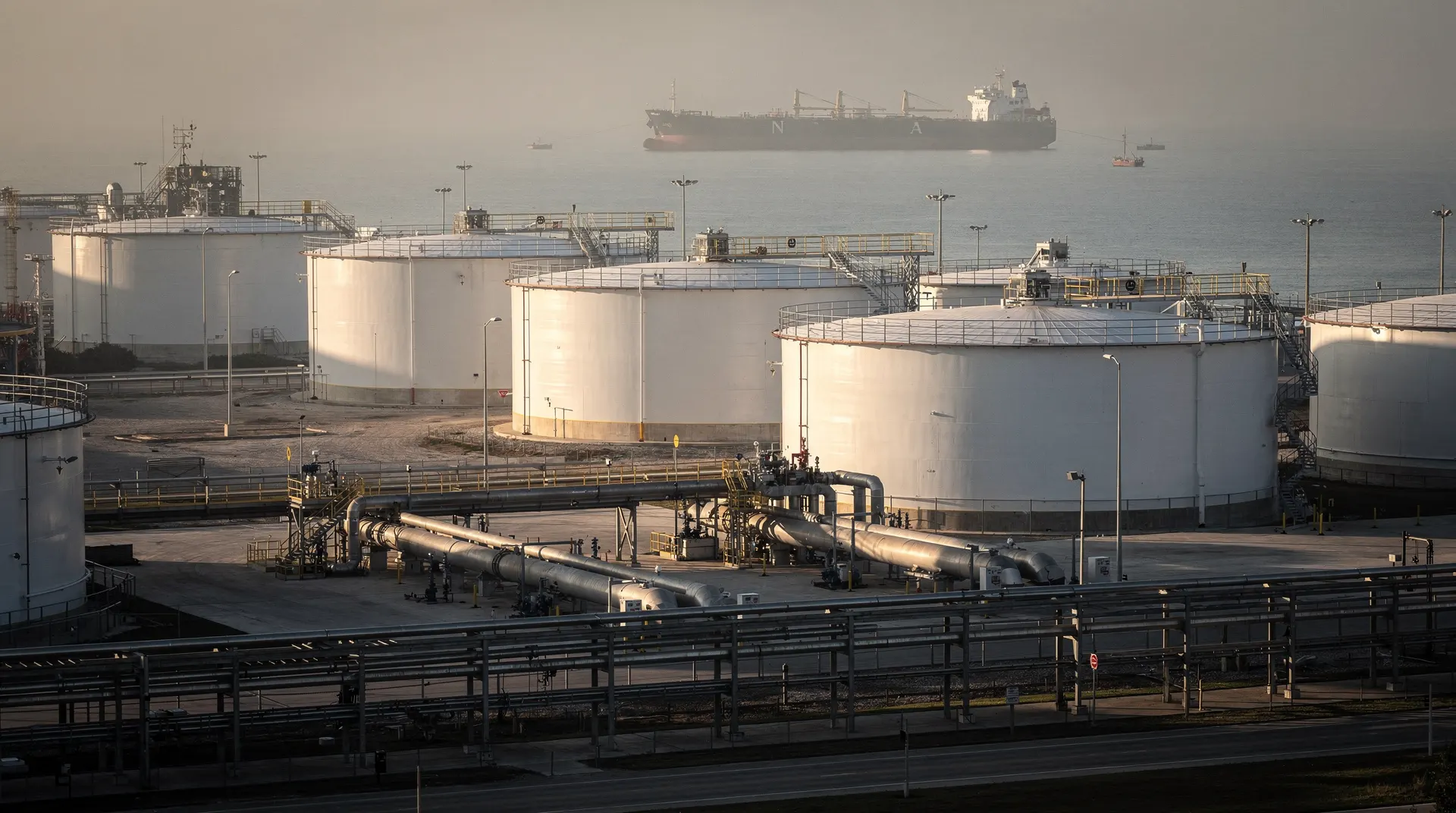 Crude oil storage tanks stand beside a Gulf Coast export berth, with a tanker in the distance.