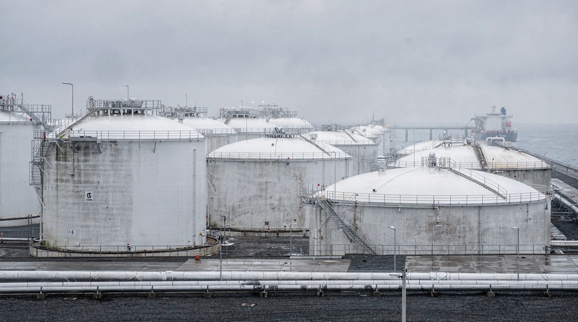 Rows of white LNG storage tanks at a coastal import terminal under an overcast winter sky
