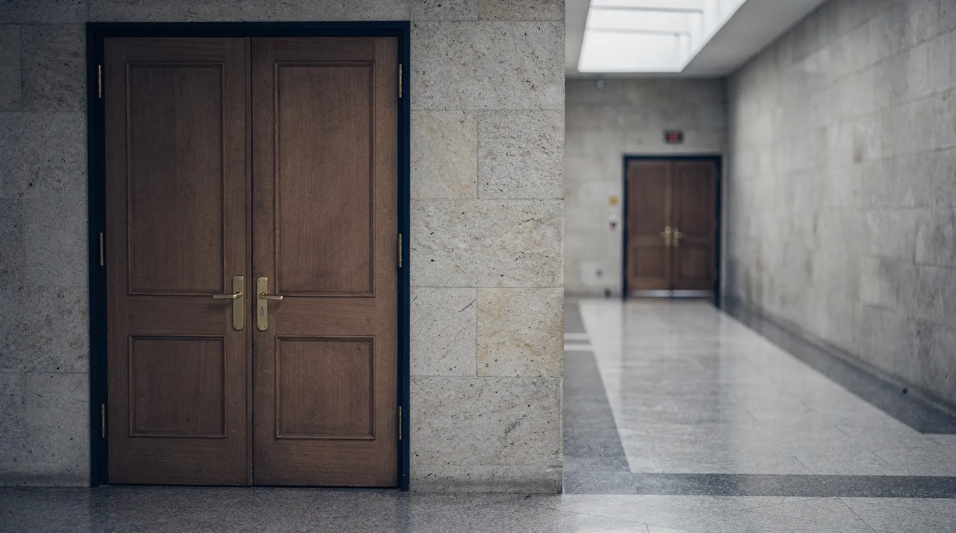 Closed meeting-room doors line a quiet stone corridor, with a second doorway visible in the distance.