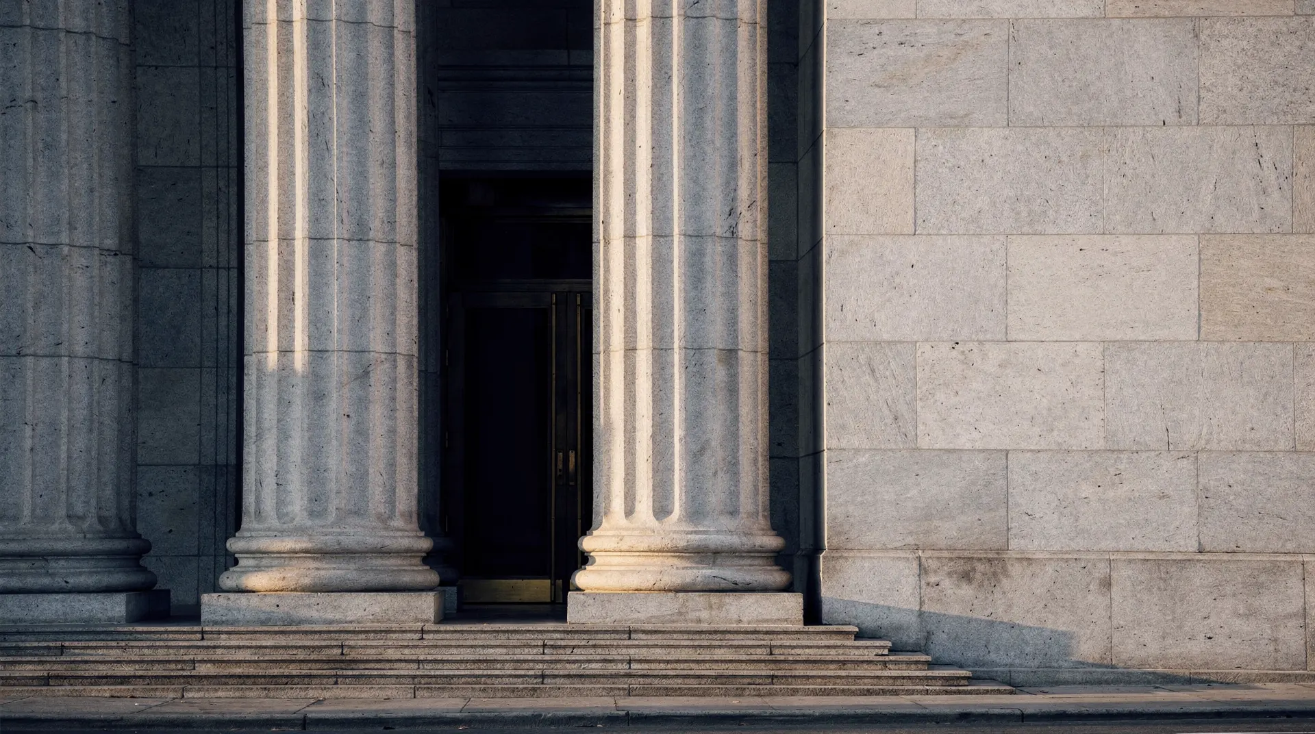 Unmarked stone columns frame the recessed entrance of a central-bank-style building in late-afternoon light.