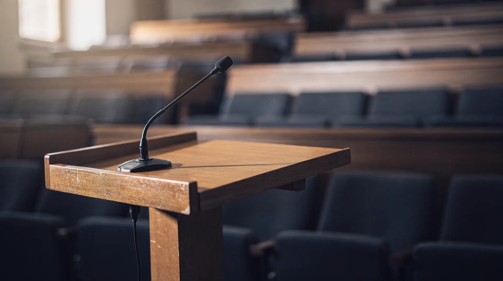 An empty lecture-hall lectern and microphone stand before rows of vacant seats.