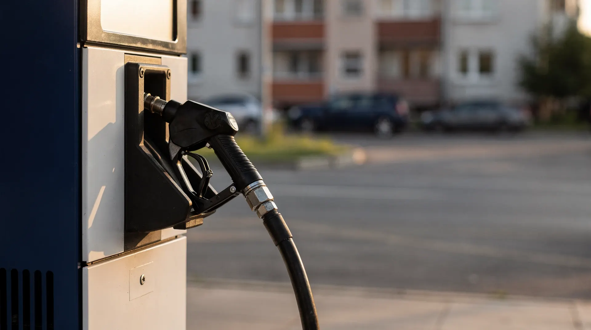 A gasoline pump nozzle sits in the foreground, with apartment buildings softly visible across the street.