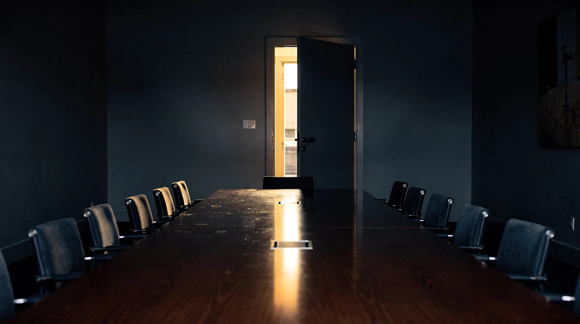 An empty conference table and vacant chairs sit before a slightly ajar door.