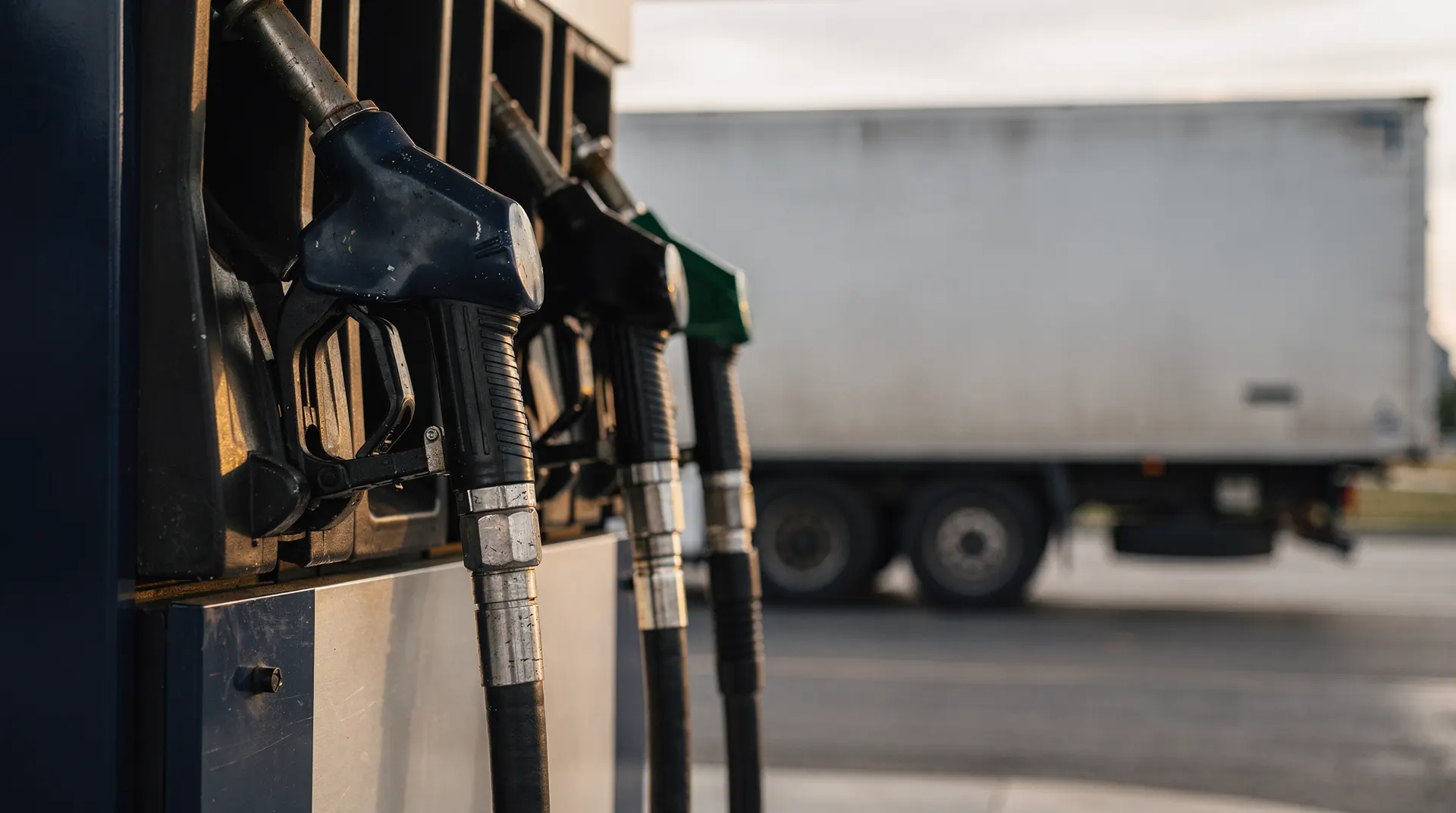Two fuel-pump nozzles in sharp focus, with a freight truck blurred in the background.