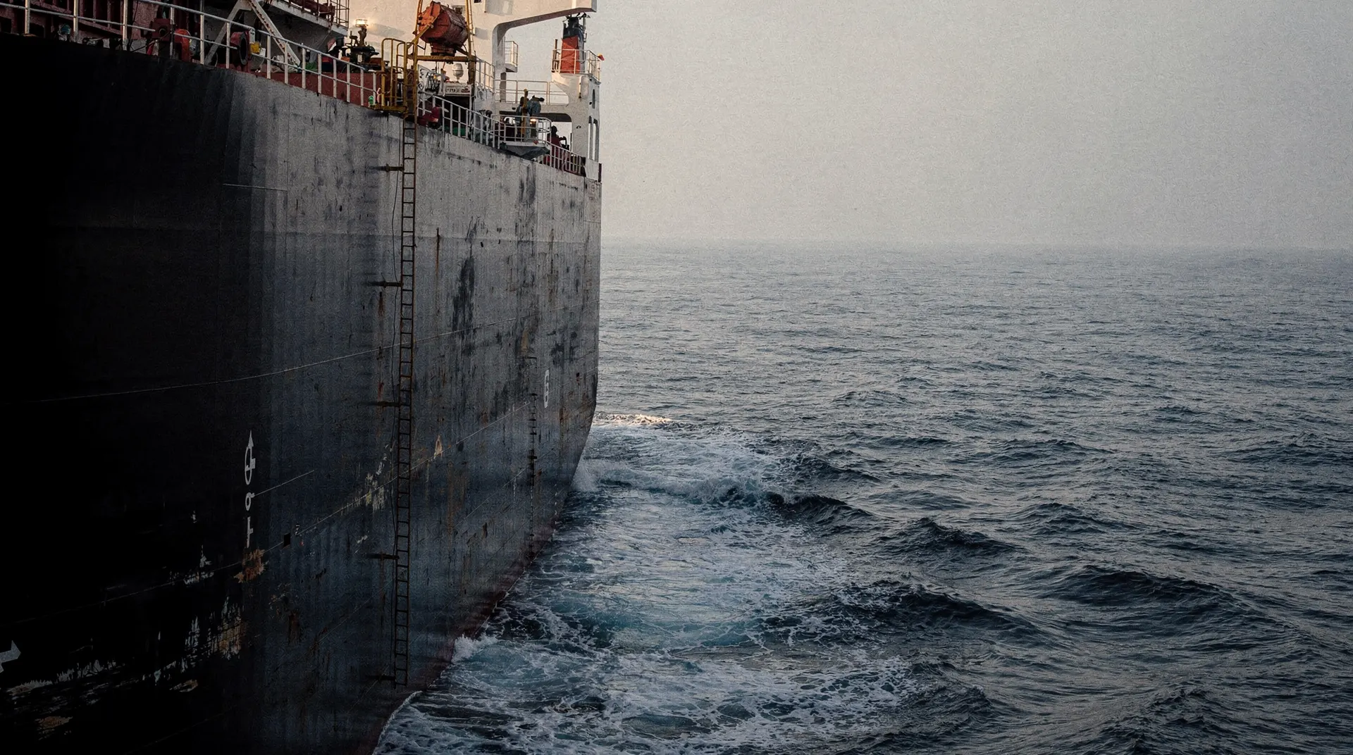 An unmarked oil tanker seen from behind its port quarter in hazy open water.