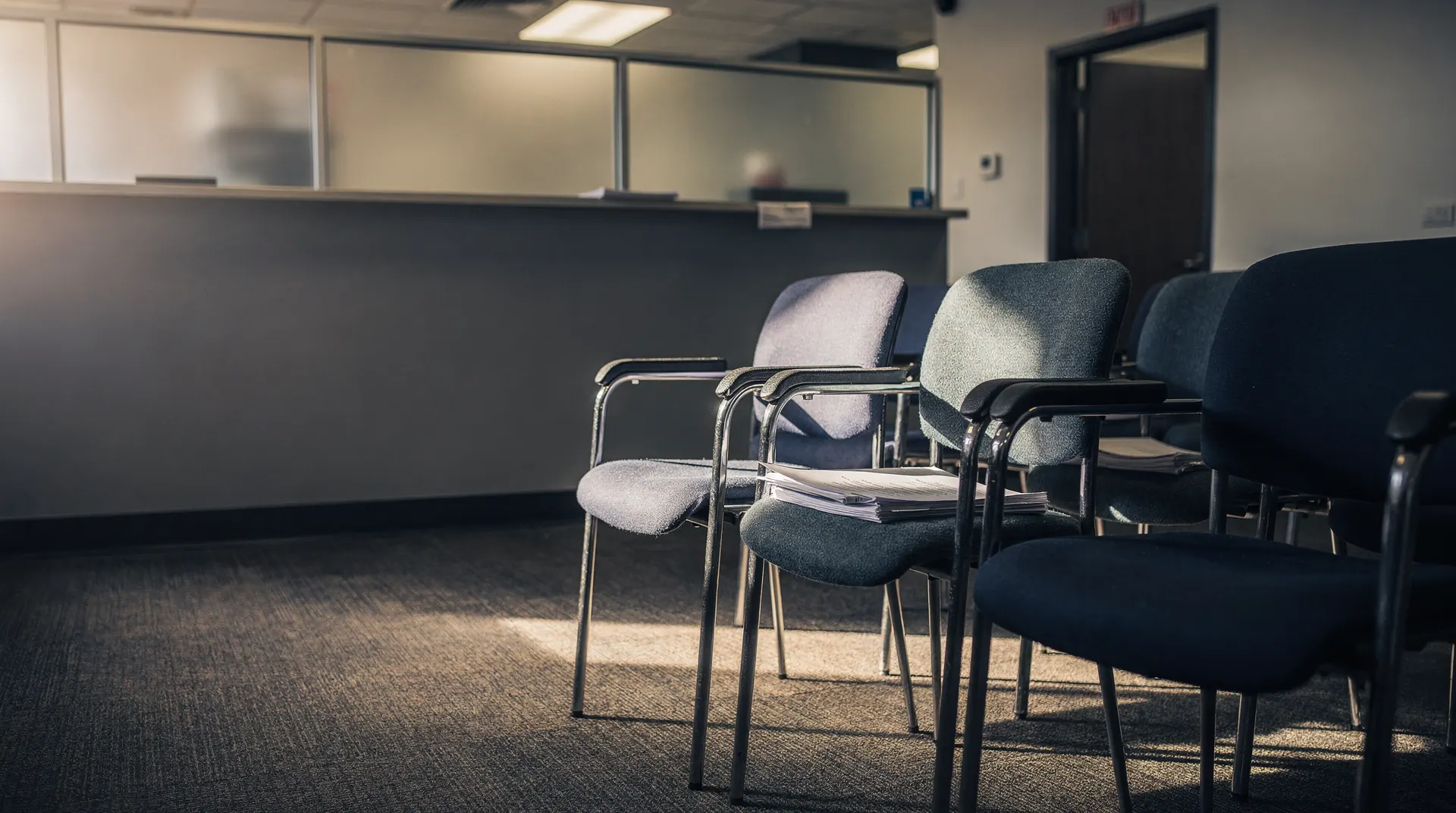 Unoccupied chairs in a quiet unemployment office waiting area, with a service counter in the background.