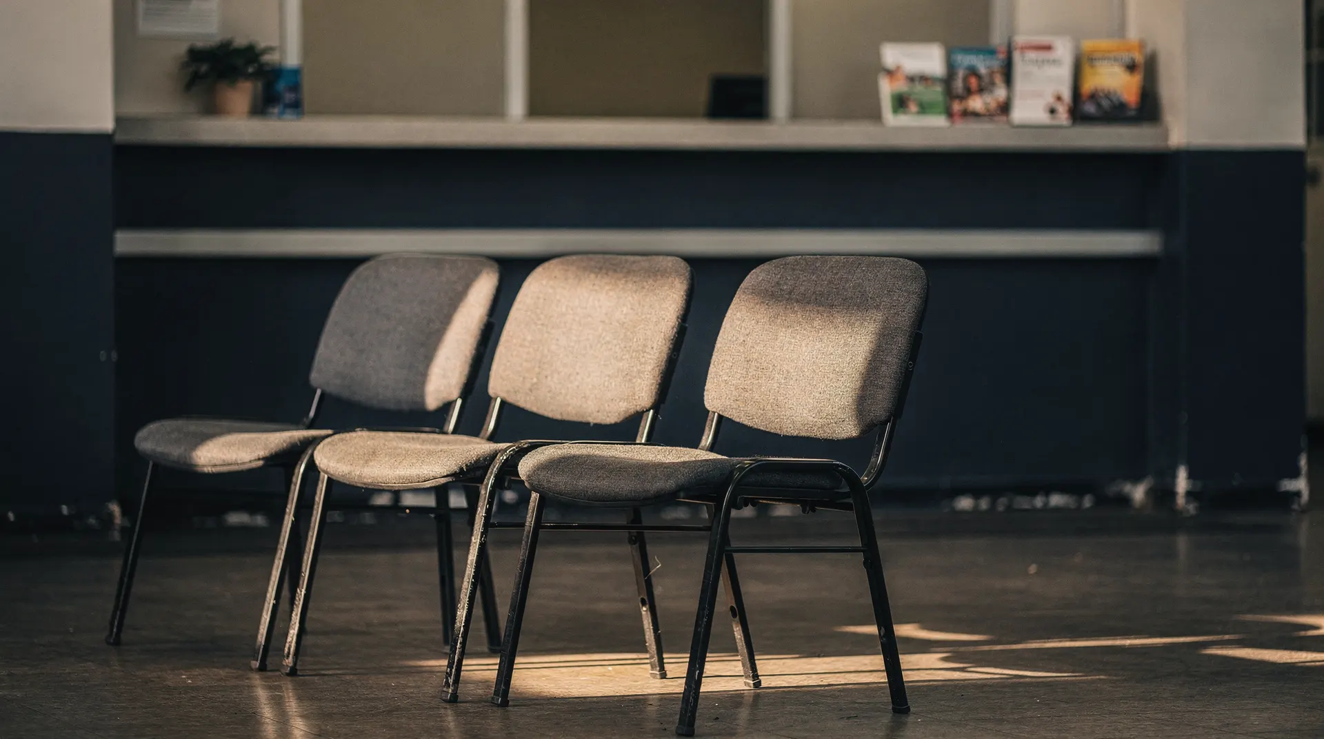 A few empty chairs face an unmarked service counter in a softly lit waiting room.