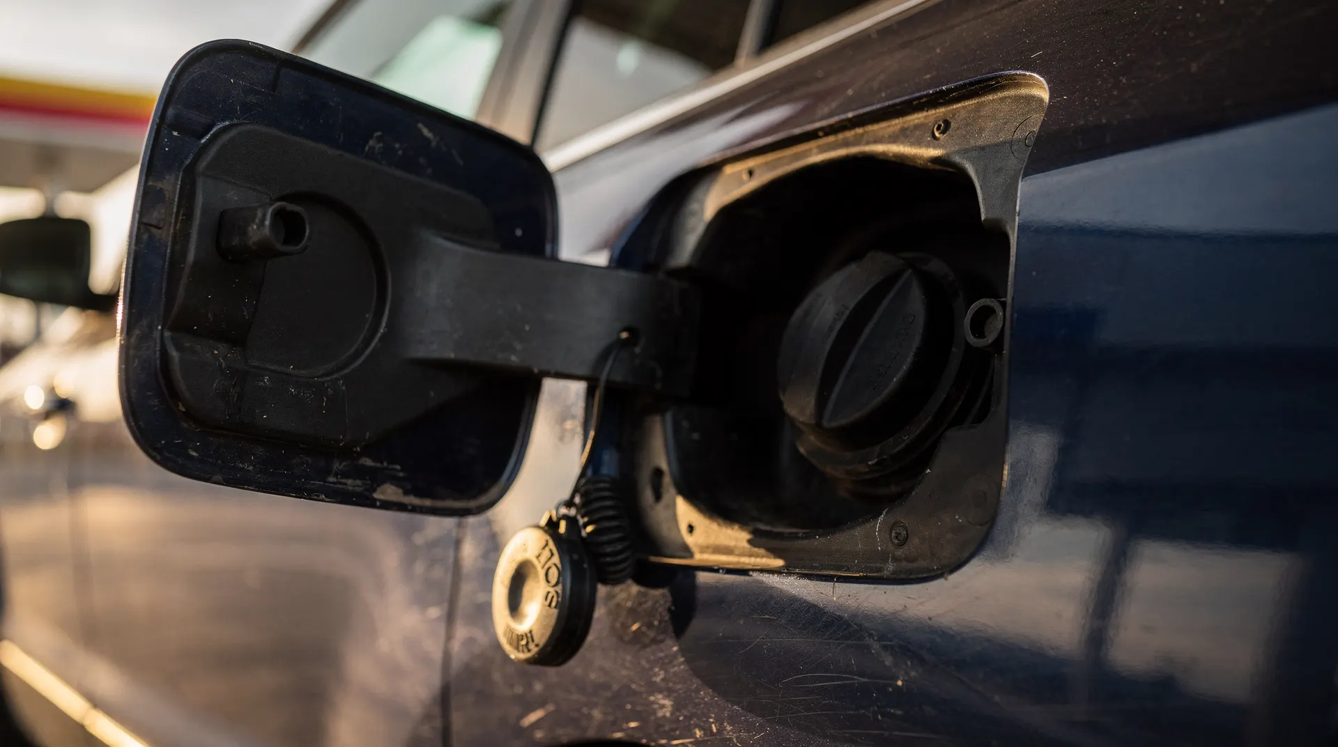 A gasoline pump nozzle rests in a vehicle fuel filler beneath a softly blurred station canopy.