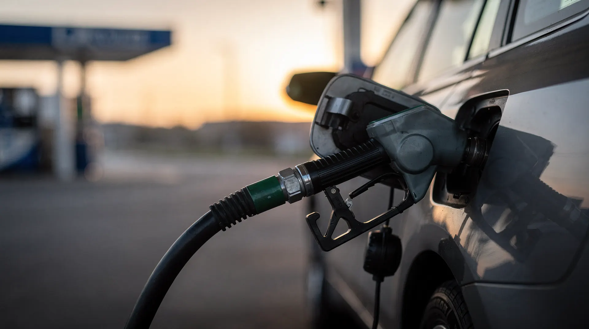 A fuel-pump nozzle rests in a car's fuel port at a quiet filling station at dawn.