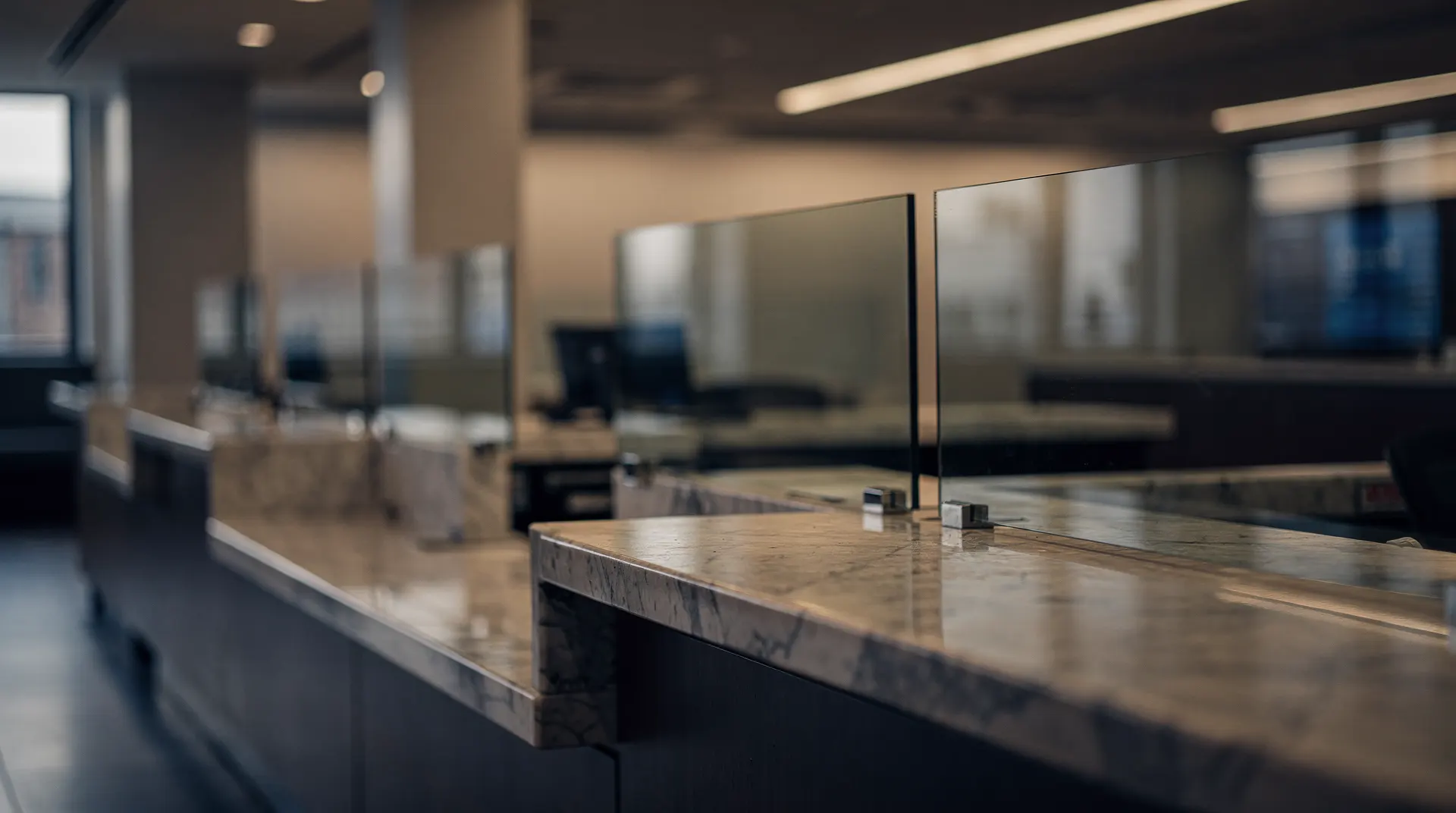 Empty bank teller counters behind glass partitions in a softly lit branch.