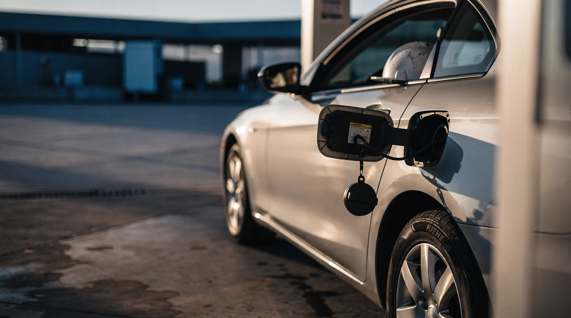 A gasoline nozzle fills a commuter car, with a hard hat visible through the passenger window.