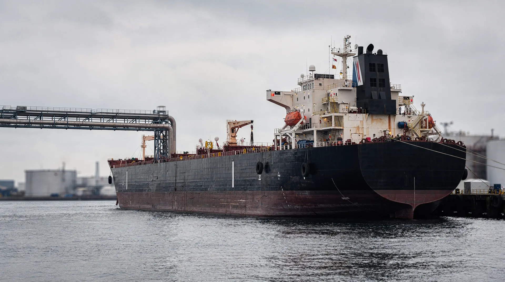 Unmarked crude-oil tanker alongside loading arms at a quiet oil terminal.