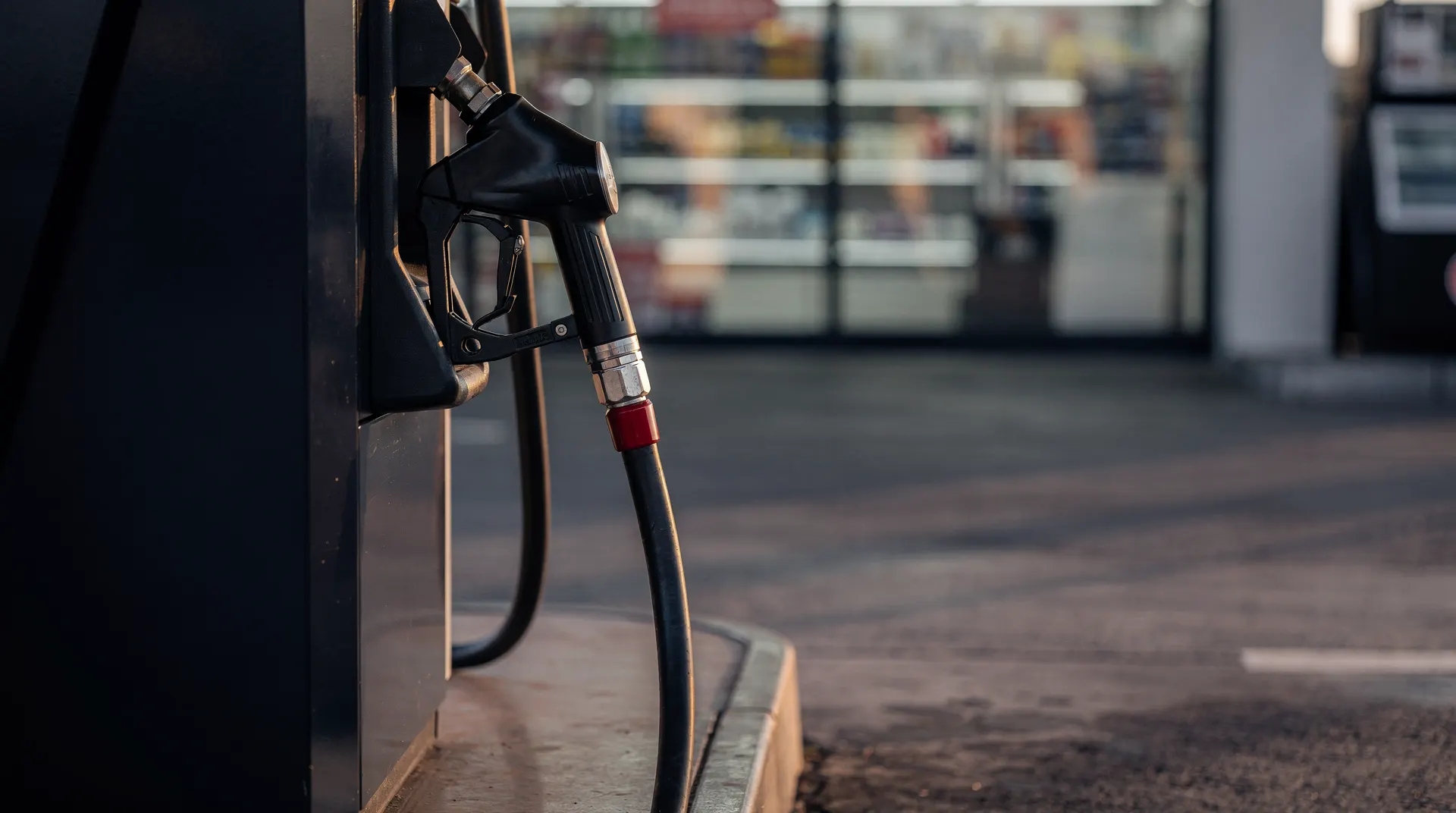 Fuel-pump nozzle in sharp focus outside a softly blurred convenience store at dawn.