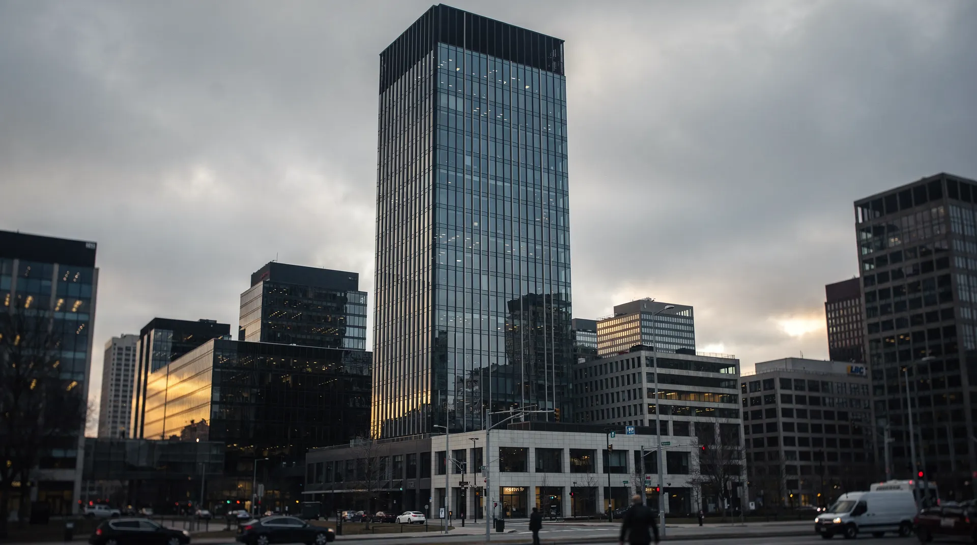 A tall glass tower looms over smaller financial-district buildings beneath an overcast sky.