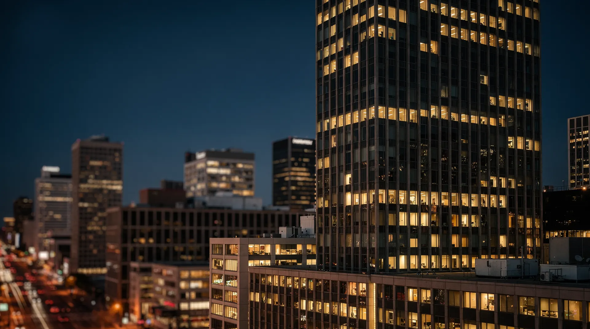 A skyscraper rises above neighboring office buildings against a dusk sky.