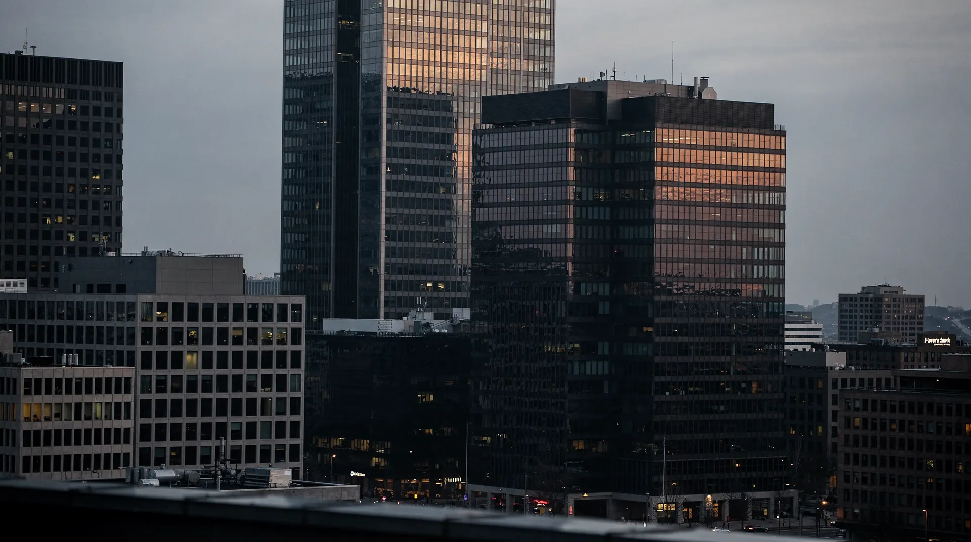 A few tall office towers catch dusk light above smaller buildings fading into shadow.