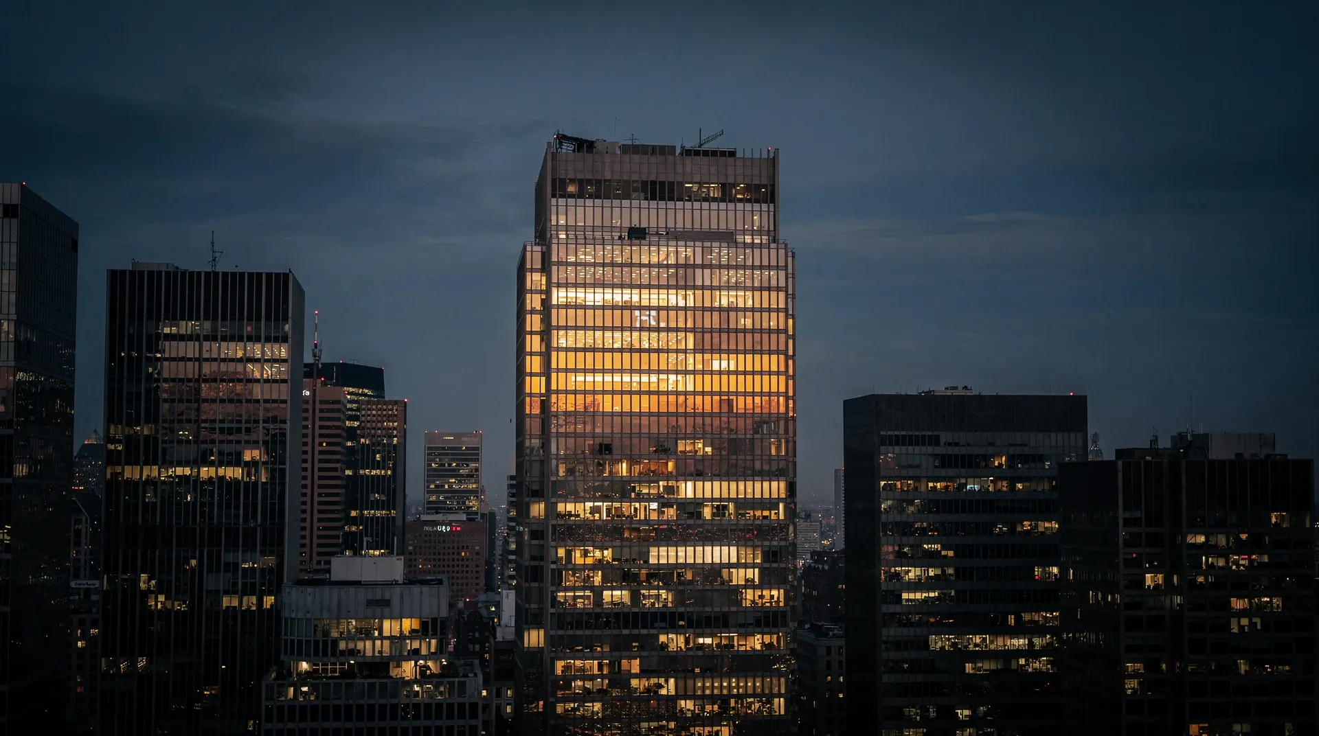 a single brightly lit glass office tower among dimmer ones