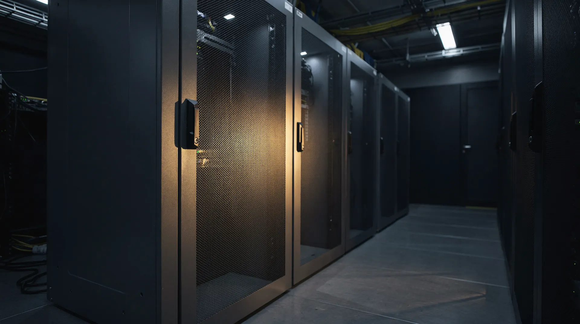One server rack catches warm light as rows of closed cabinets recede into a dim data-center aisle.