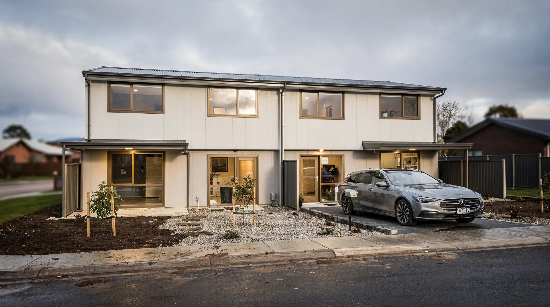 A newly built house with unfinished landscaping and a car parked in its driveway under an overcast sky.