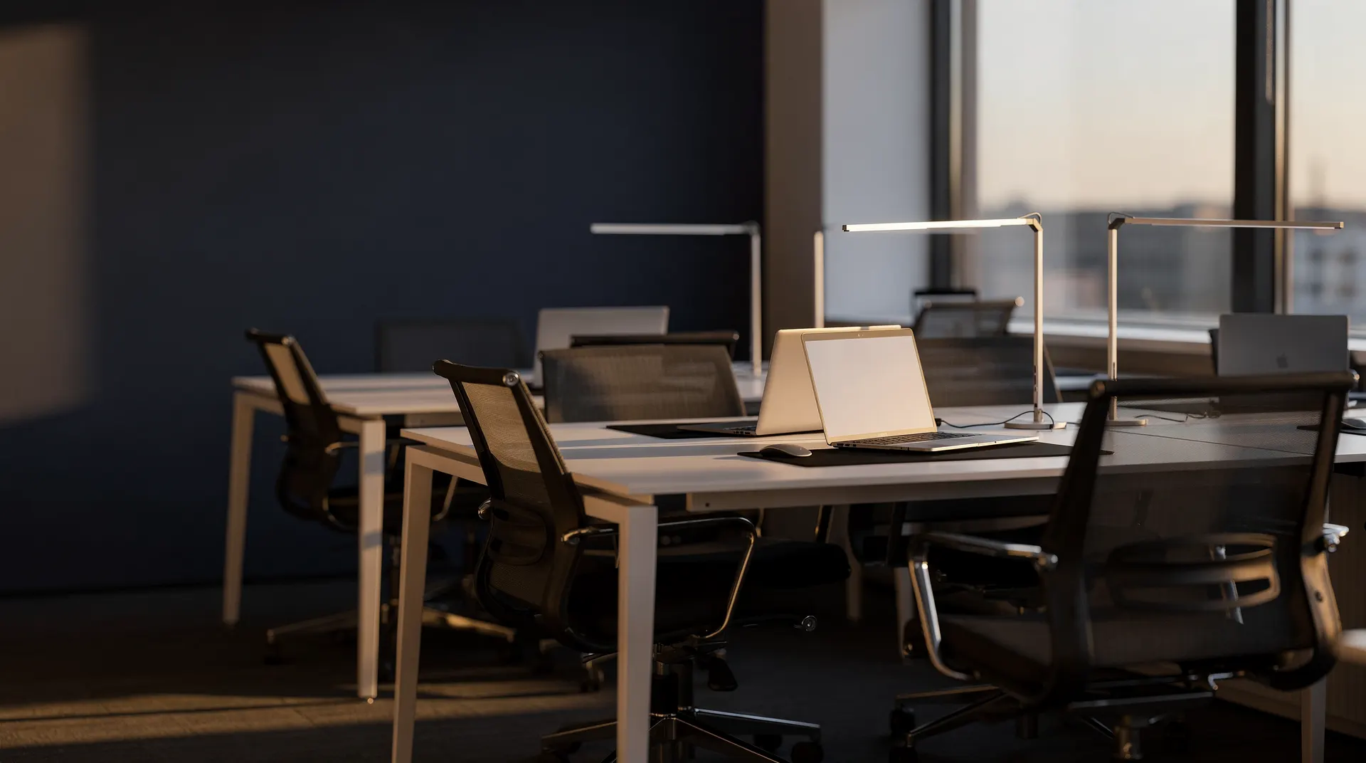 Empty office desks and chairs sit in soft morning light.